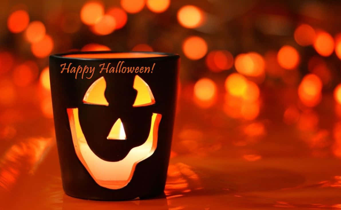 Halloween Props 桌布 壁紙 — 一個發光的黑色萬聖節燭台，帶有傑克南瓜燈的臉和「Happy Halloween!」文字，背景是溫暖的散景。