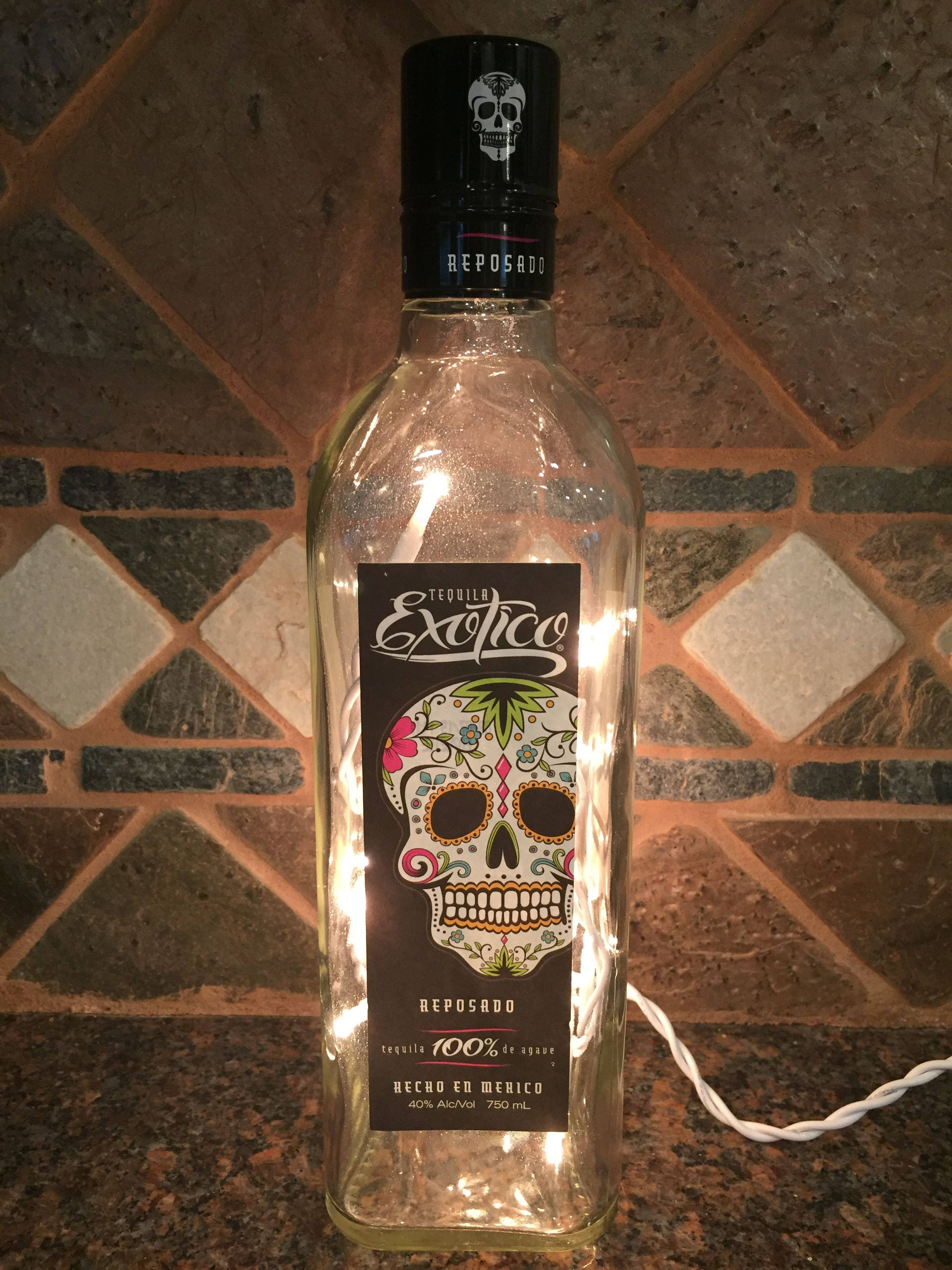 bottle 桌布 壁紙 — 一個發光的龍舌蘭酒瓶，帶有彩色糖骷髏標籤，放在瓷磚檯面上，由串燈照亮。
