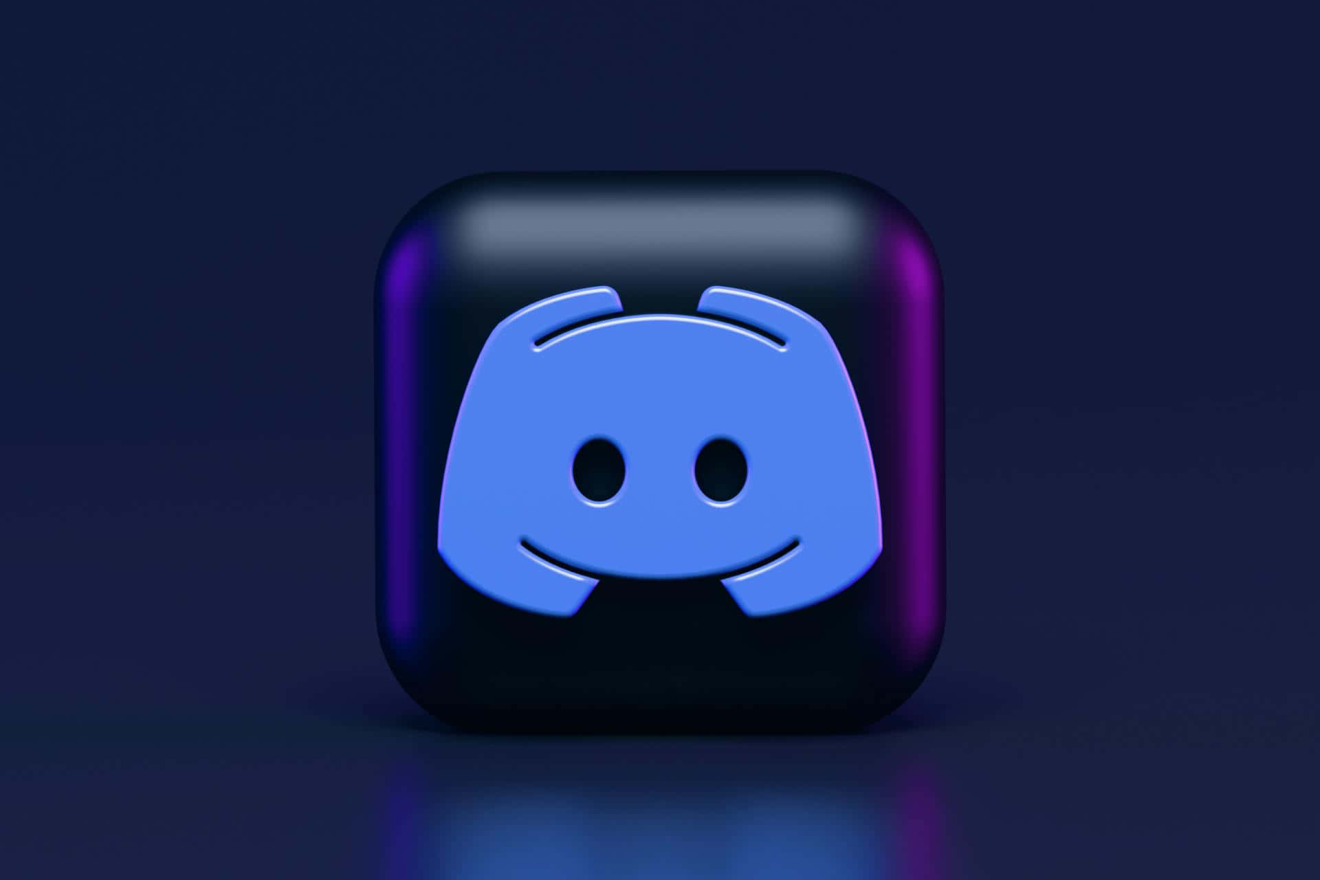 Discord Logo 桌布 壁紙 — 一個發光藍色Discord標誌圖標，帶有紫色亮點，在戲劇性燈光下居中放置在深色反光表面上。