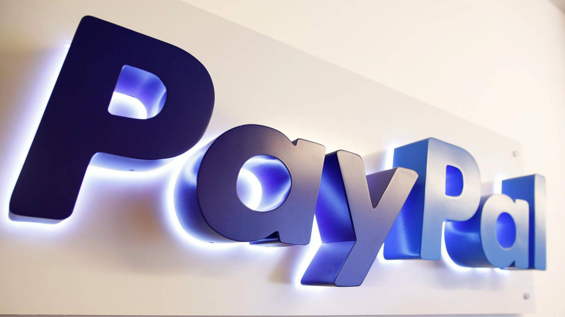 PayPal 桌布 壁紙 — 一個發光藍色PayPal標誌的特寫，安裝在白色牆壁上，帶有柔和背光。