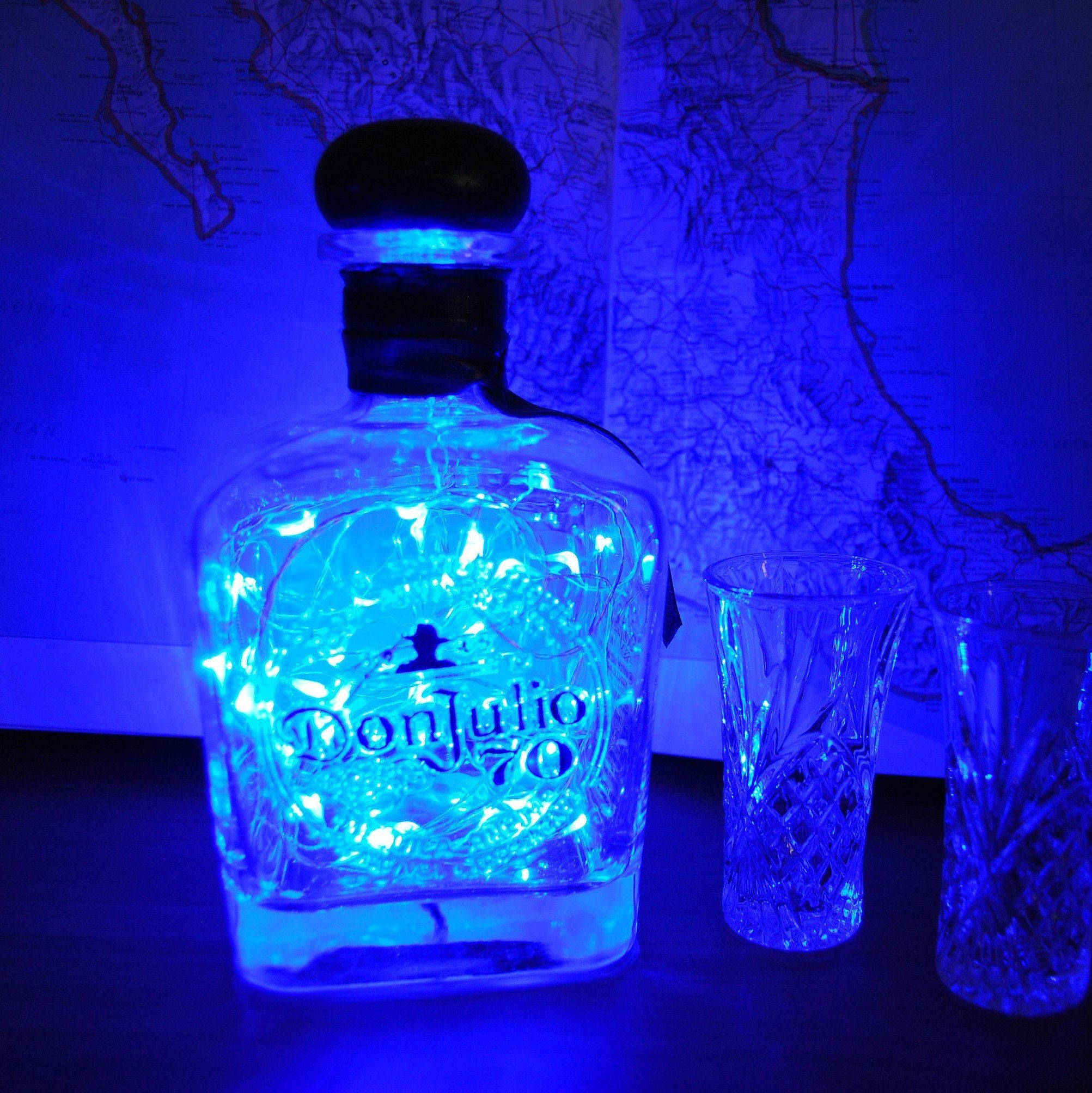glass 桌布 壁紙 — 一個發光藍色燈串的Don Julio 70龍舌蘭酒瓶放在地圖背景旁的水晶杯旁邊。