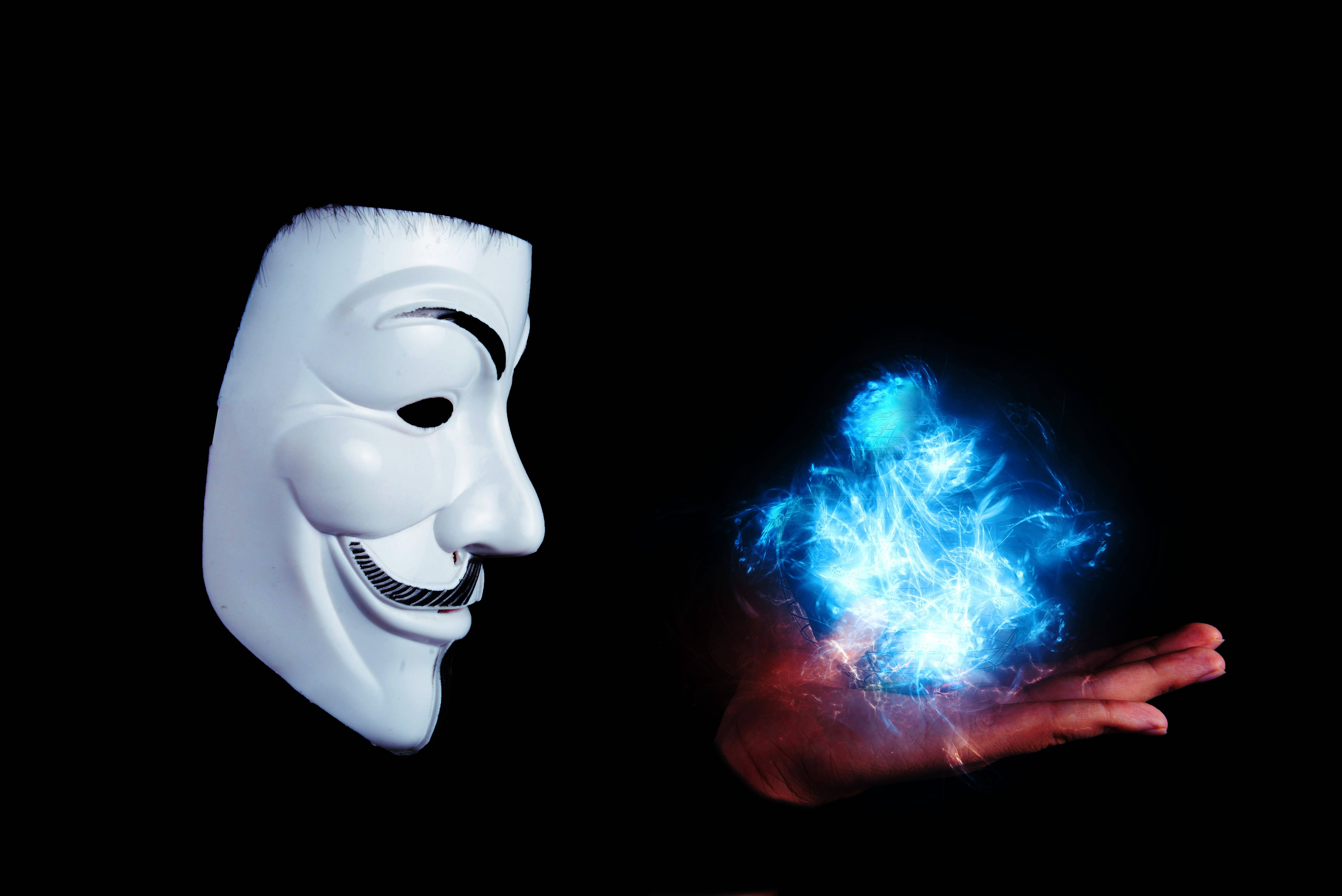 Flame 桌布 壁紙 — 一個白色 Guy Fawkes 面具凝視著一隻伸出的手中握著的發光藍色能量球，背景為黑色。