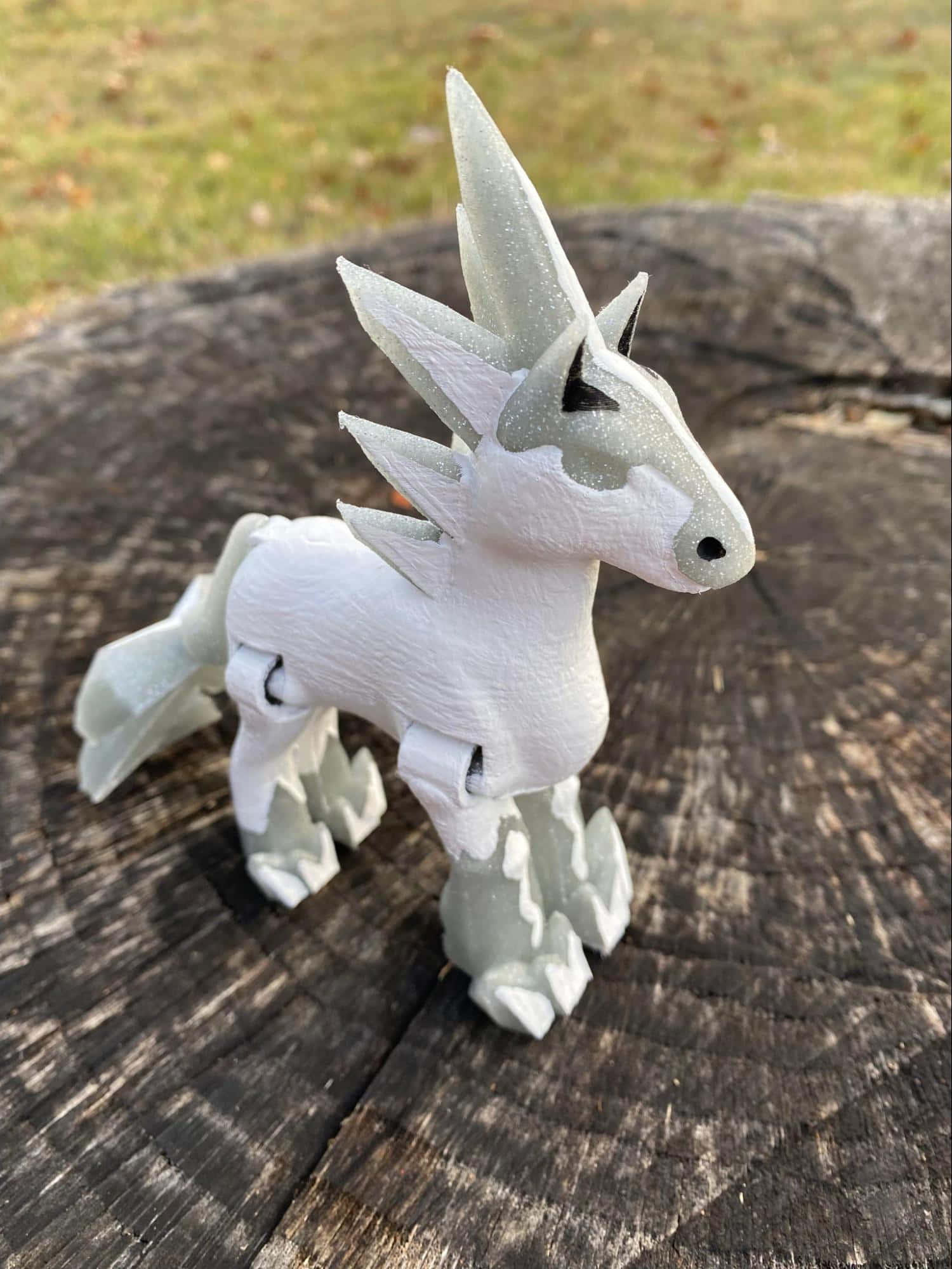 寶可夢 桌布 壁紙 — 一個白色3D列印風格化的獨角獸雕像，帶有閃閃發光的角，站在戶外一個風化的樹樁上。