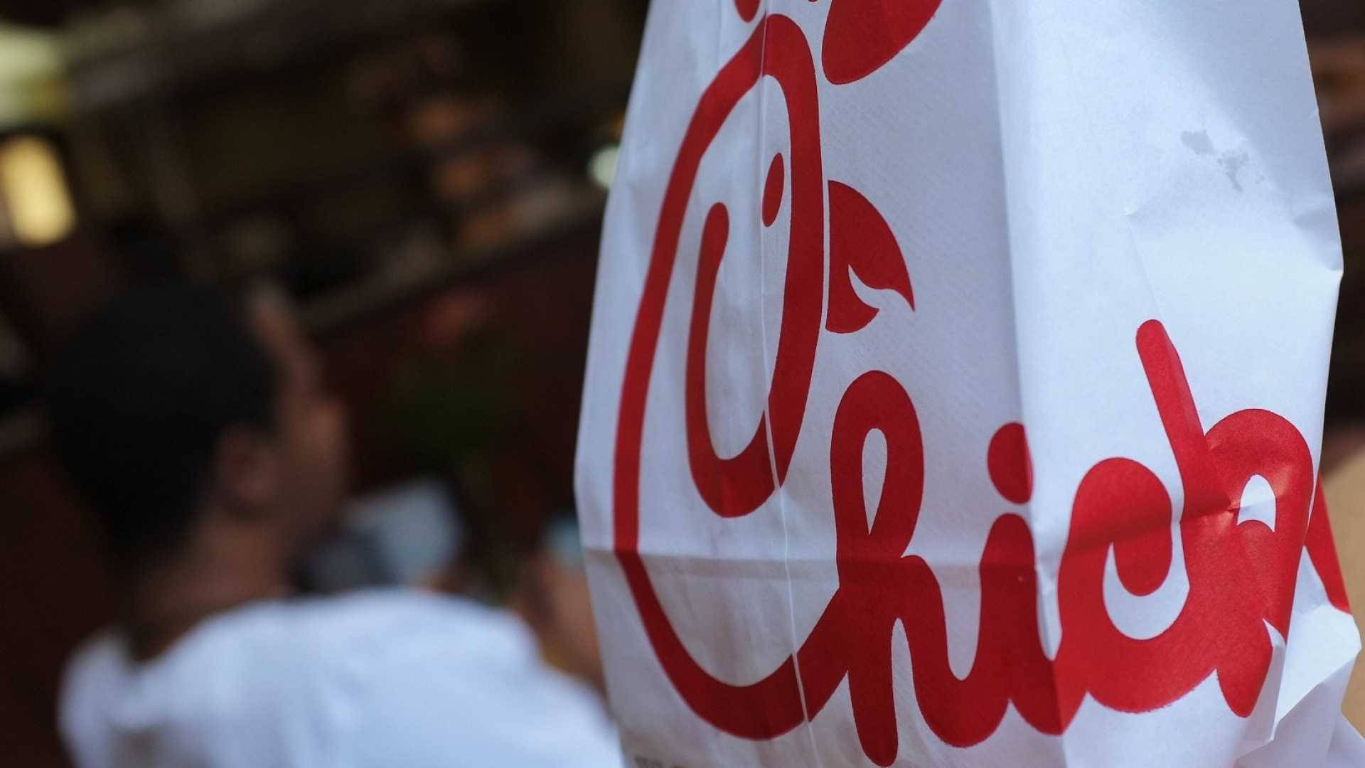 chick 桌布 壁紙 — 一個白色Chick-fil-A紙袋的特寫，前景有粗體紅色標誌，背景有模糊的人影。