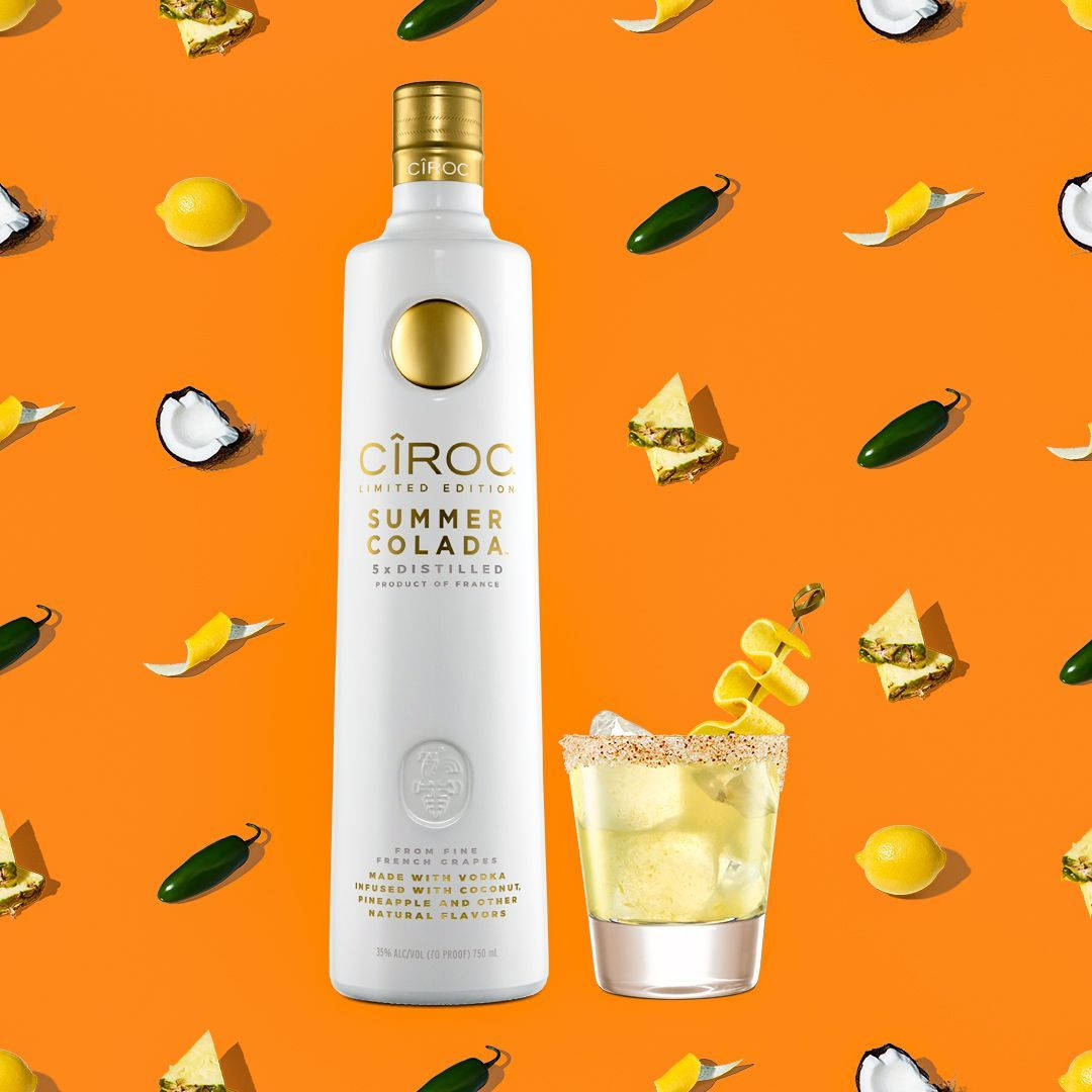飲料 桌布 壁紙 — 一個白色Ciroc Summer Colada伏特加酒瓶和雞尾酒杯，周圍散落著熱帶水果，背景為鮮豔的橙色。