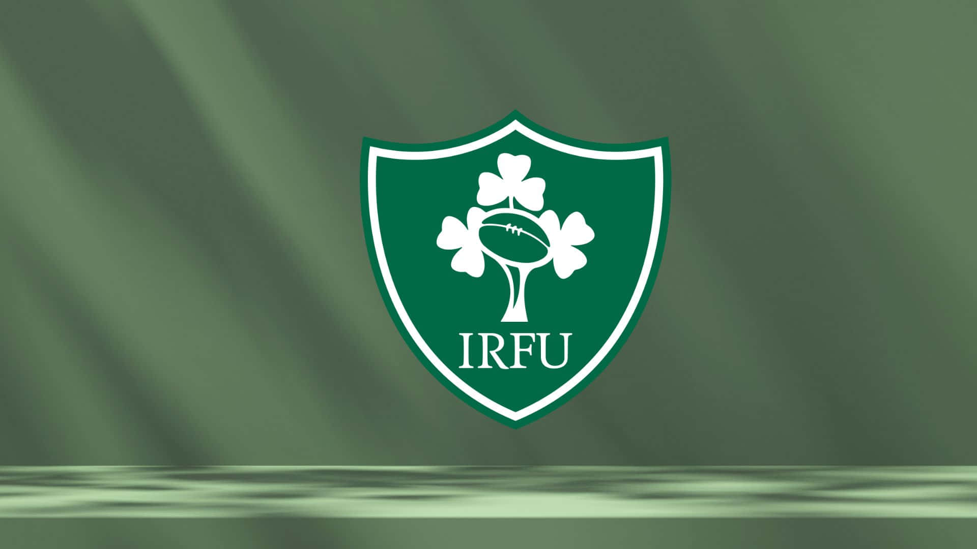 Ireland Rugby 桌布 壁紙 — 一個白色IRFU橄欖球徽章，中心有一個三葉草和一個球，背景是帶紋理的綠色旗幟。