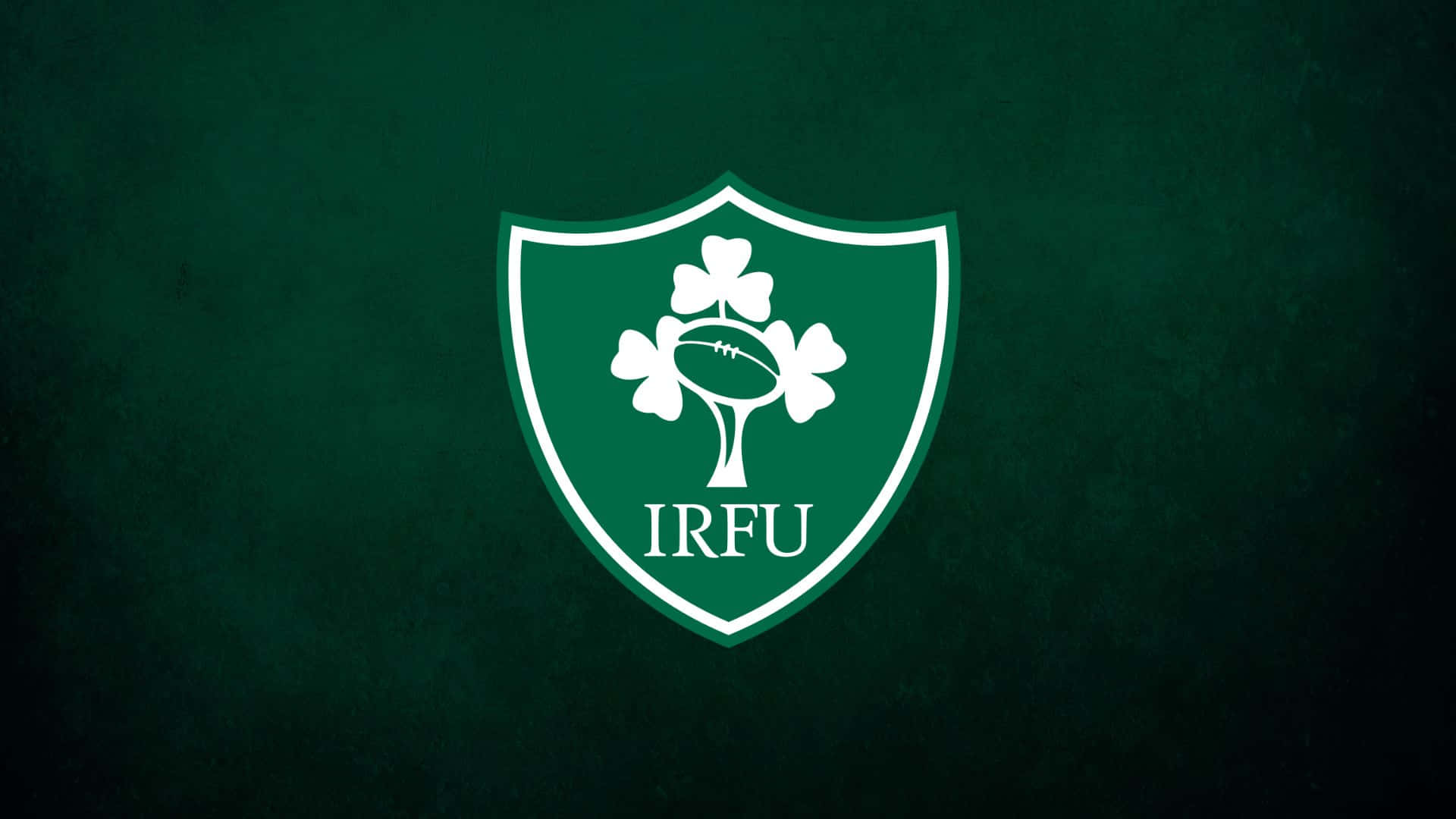 Ireland Rugby 桌布 壁紙 — 一個白色IRFU盾牌標誌，中央有酢漿草和橄欖球，置於有紋理的深綠色背景上。