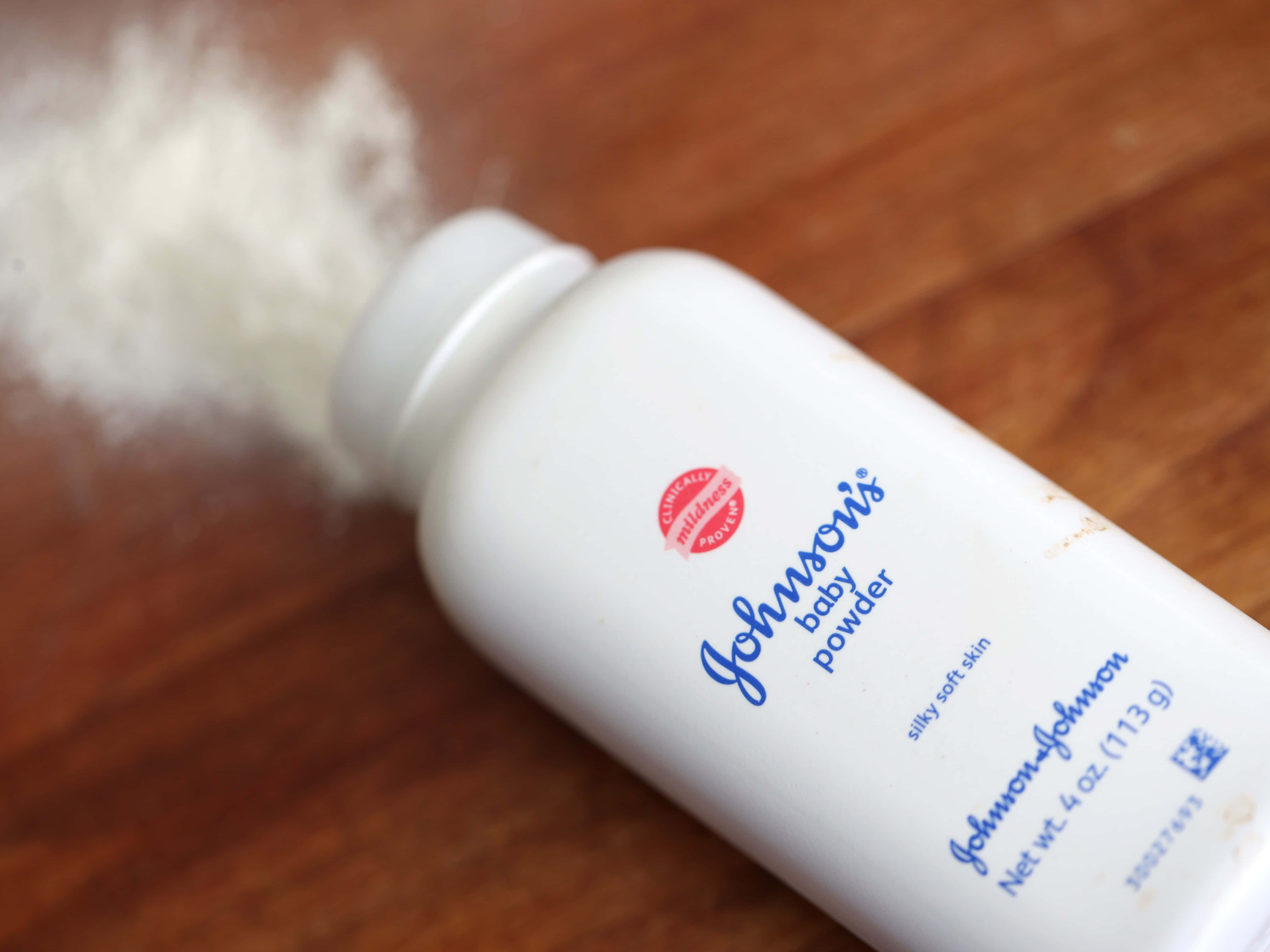 Baby Powder 桌布 壁紙 — 一個白色Johnson's嬰兒爽身粉瓶在木質表面上傾倒，細微的粉末雲向上飄散。