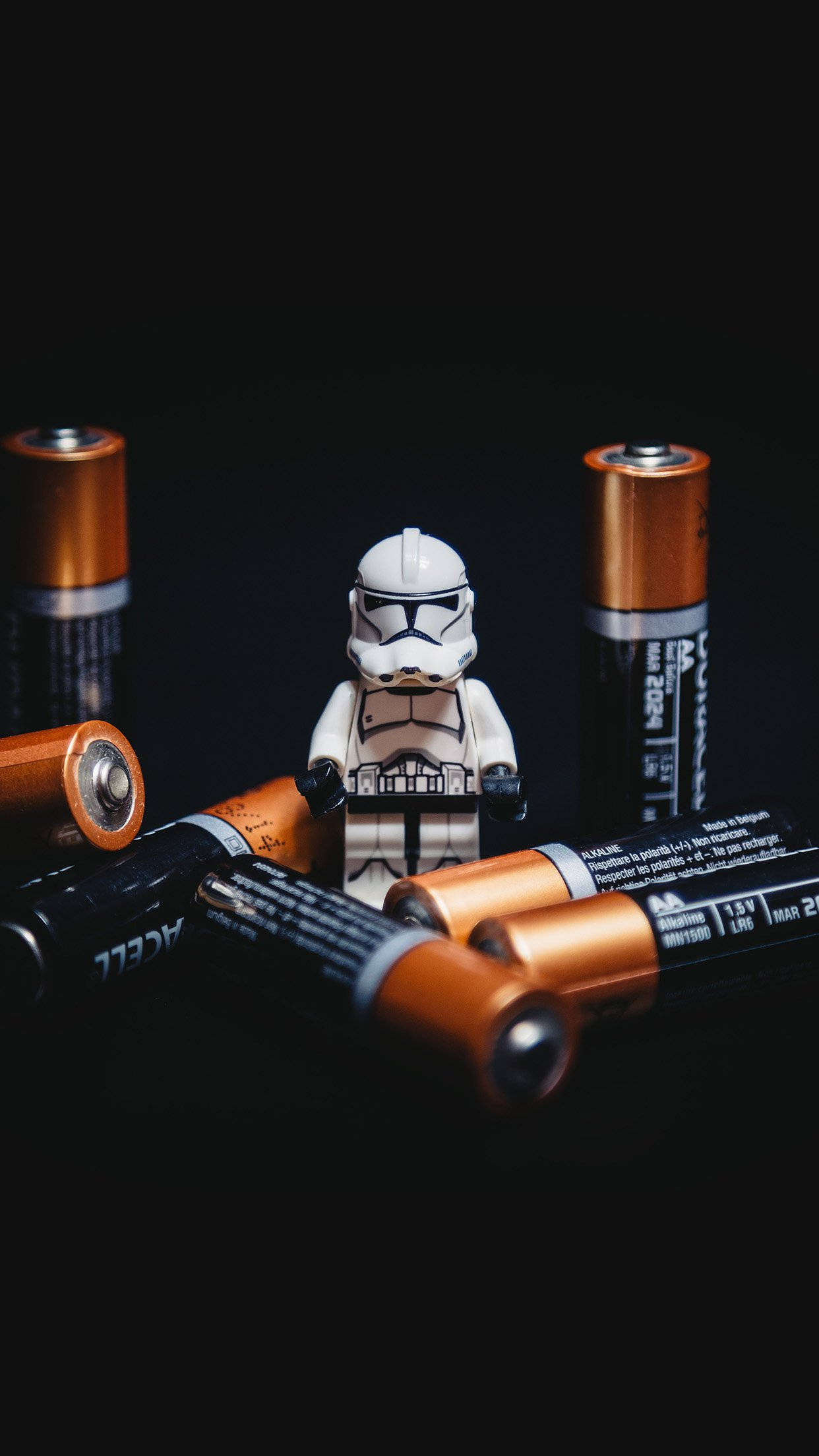 Smartphone 桌布 壁紙 — 一個白色LEGO風暴兵人偶站在散落的AA電池中央，背景為純黑色。