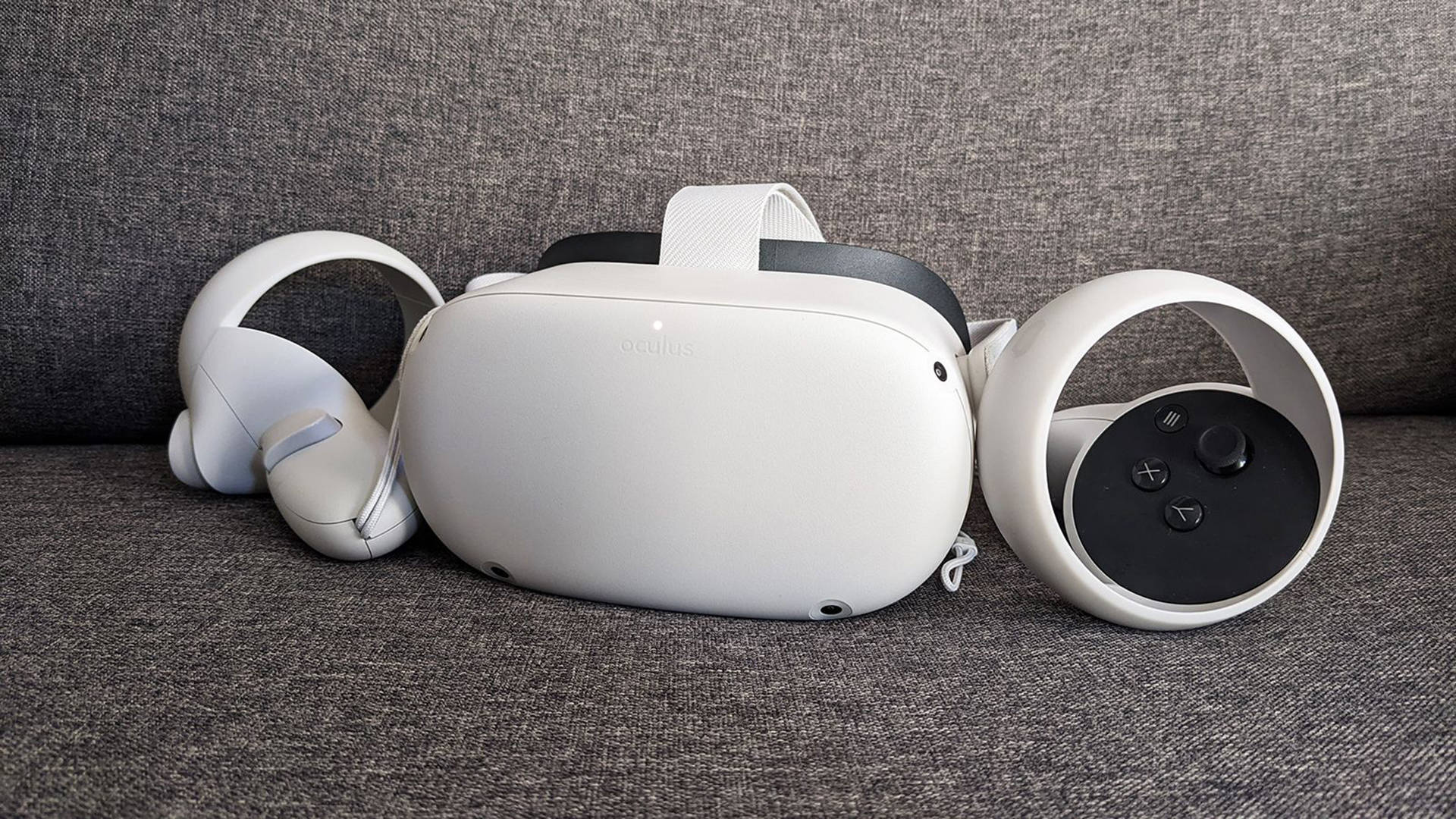 Quest 桌布 壁紙 — 一個白色Oculus VR頭戴式裝置和控制器整齊地放在一張有紋理的灰色布沙發上。