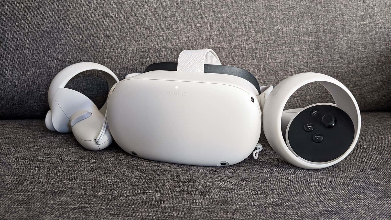 Oculus Quest 2 桌布 壁紙 — 一個白色Oculus VR頭戴式裝置和控制器整齊地放在一張有紋理的灰色布沙發上。