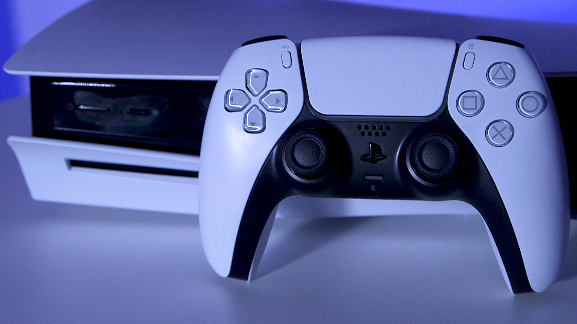 PS5 動態圖片 桌布 壁紙 — 一個白色PlayStation 5手把放在主機前，在冷藍色燈光下。