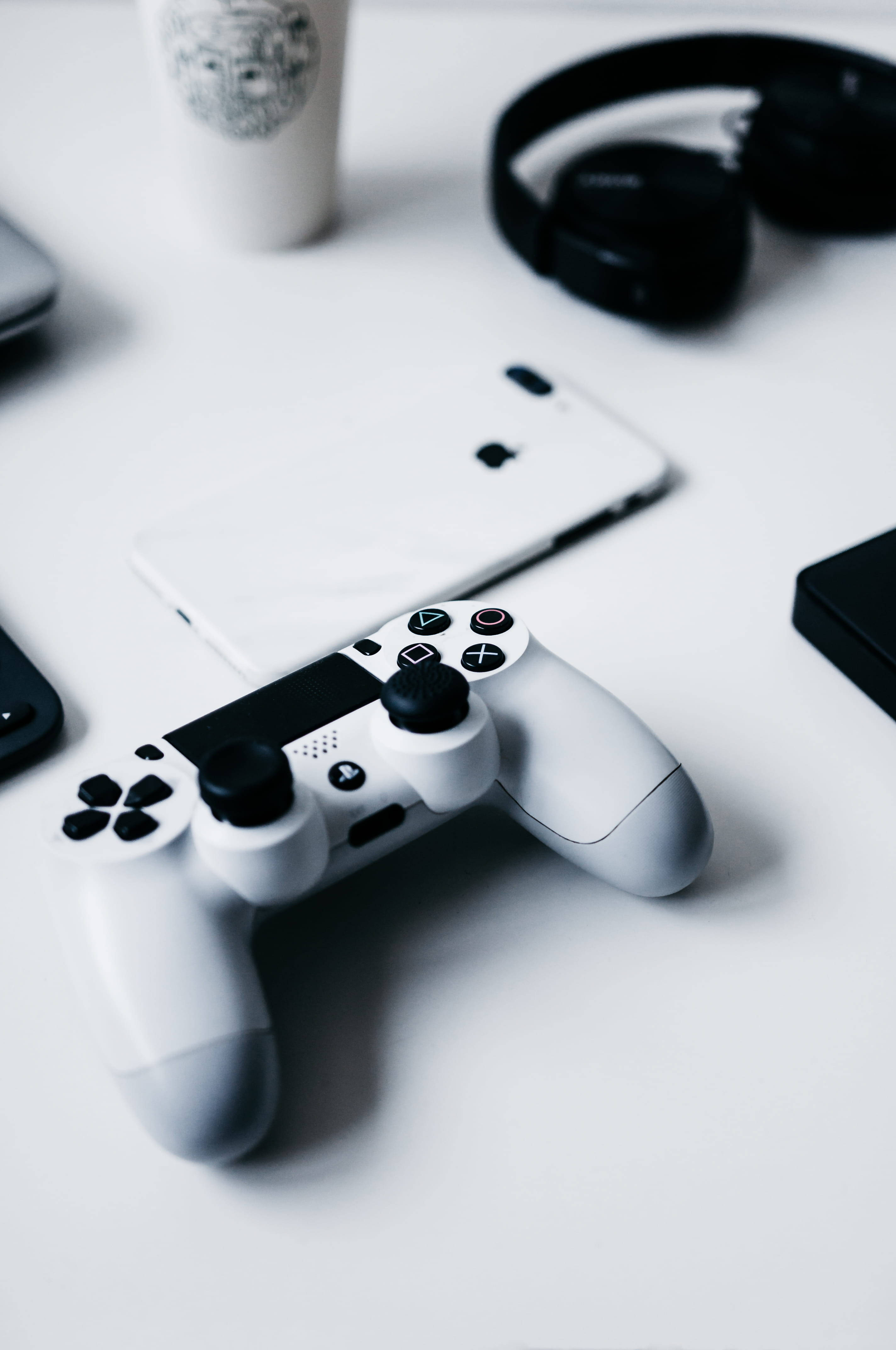 PlayStation 桌布 壁紙 — 一個白色PlayStation手把放在乾淨的白色桌子上，旁邊有耳機和一杯咖啡，呈現柔和的單色調。