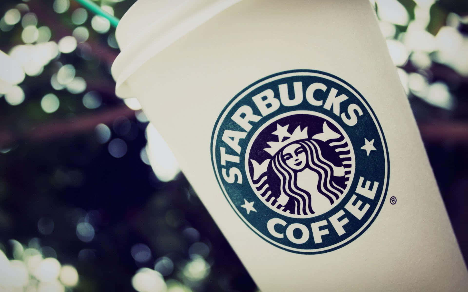 星巴克 桌布 壁紙 — 一個白色Starbucks咖啡杯的特寫，帶有其標誌性的海妖標誌，背景是模糊的綠色散景。
