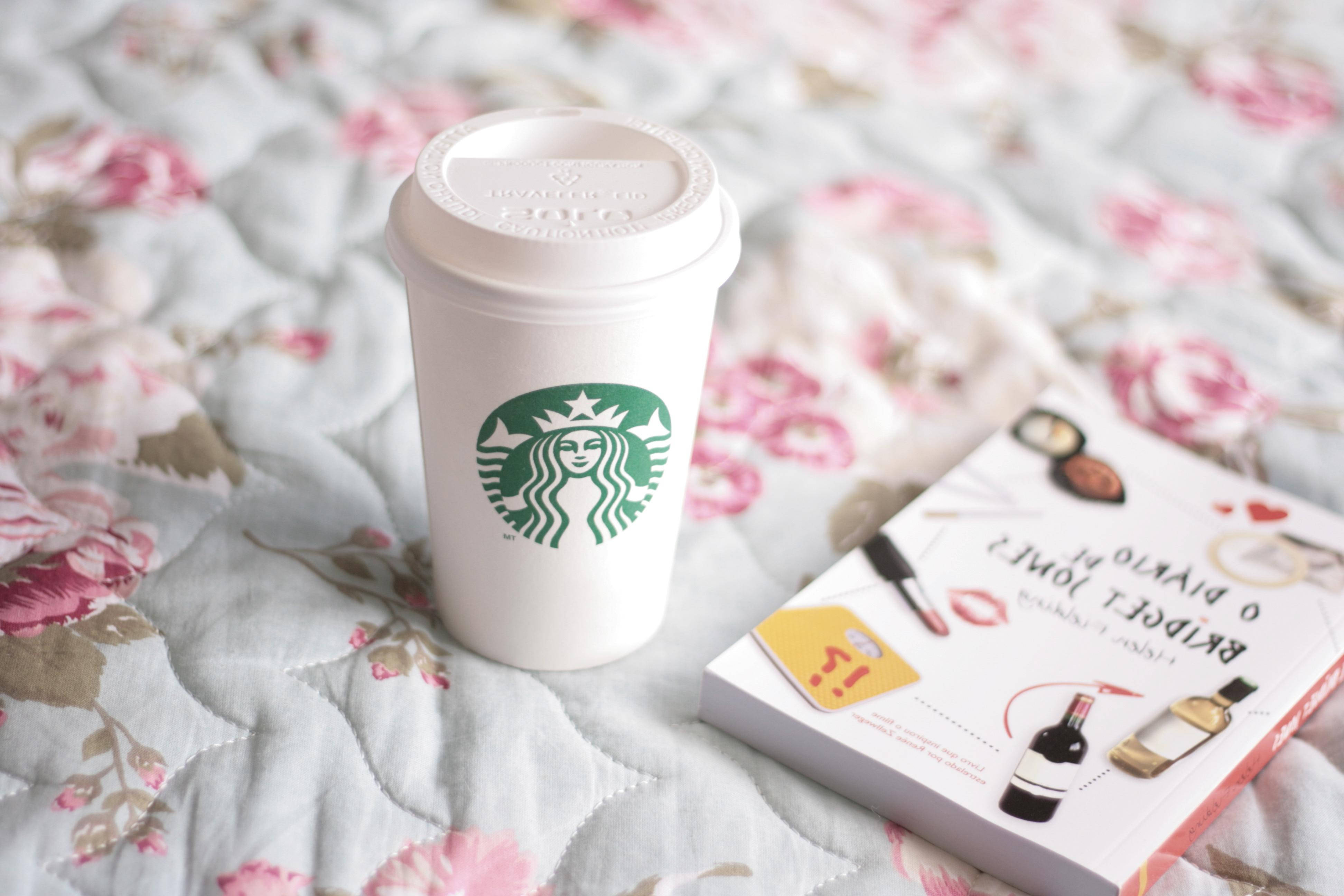 星巴克 桌布 壁紙 — 一個白色Starbucks杯和一本書放在花卉絎縫床罩上，柔和自然光線中。