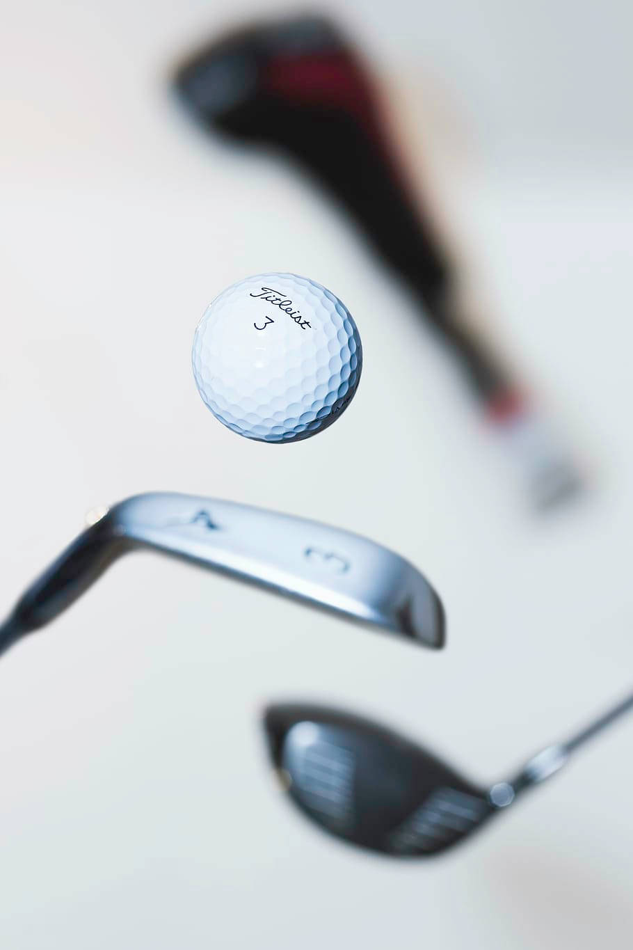 高爾夫 桌布 壁紙 — 一個白色Titleist高爾夫球在模糊的高爾夫球桿之間懸浮於半空，背景柔和中性。