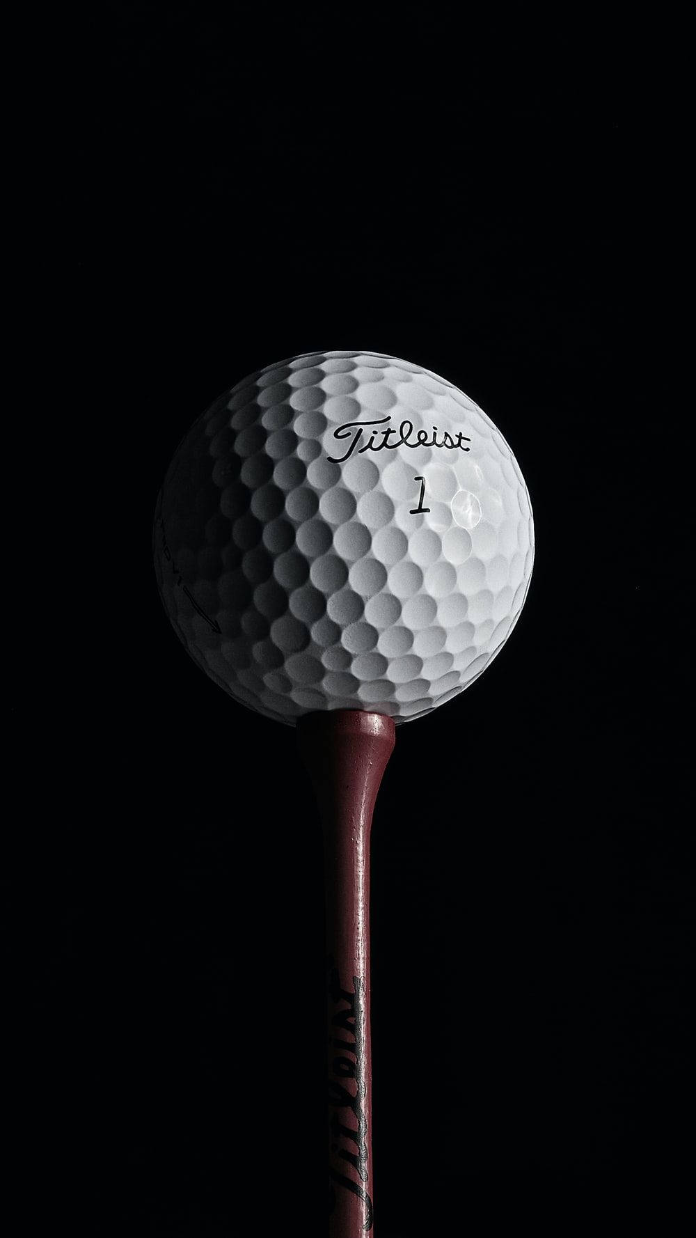 Golfing 桌布 壁紙 — 一個白色Titleist高爾夫球（一號球）放在一個栗色高爾夫球座上，背景為純黑色。