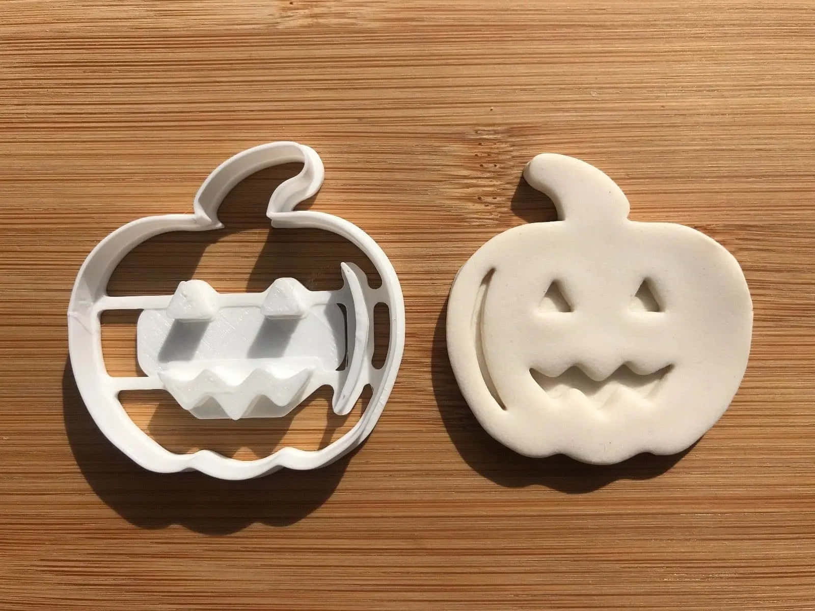Halloween Cookie Cutters 桌布 壁紙 — 一個白色南瓜形餅乾模具及其壓出的麵團印記並排放在木質表面上。