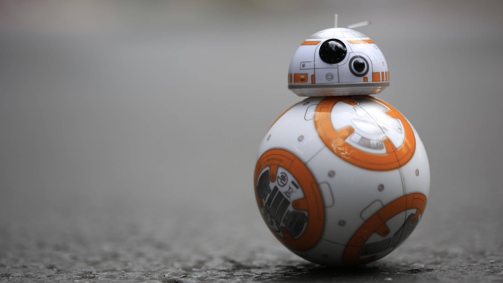 機器人 桌布 壁紙 — 一個白色和橙色的BB-8機器人站在灰色混凝土表面上，景深較淺。