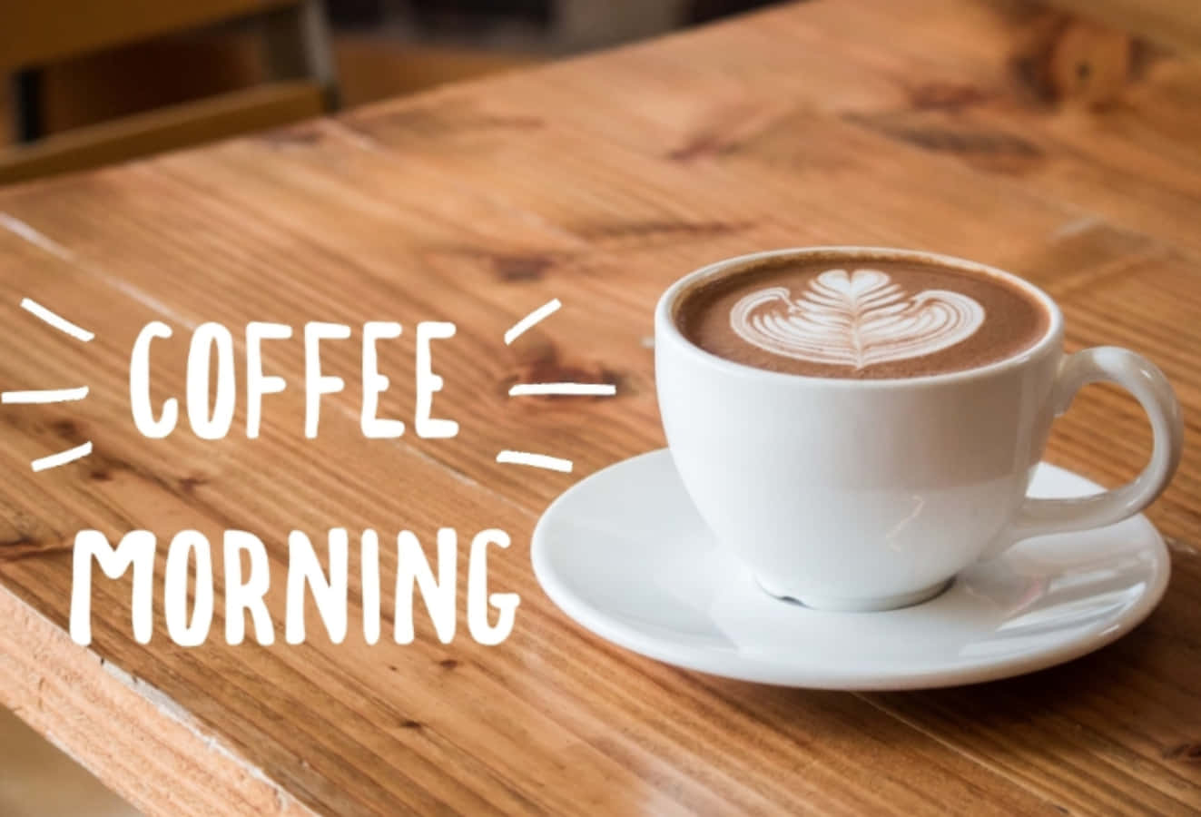 Morning Coffee 桌布 壁紙 — 一個白色咖啡杯，上面有葉子拉花藝術，放在木桌上，旁邊有粗體字寫著 coffee morning。