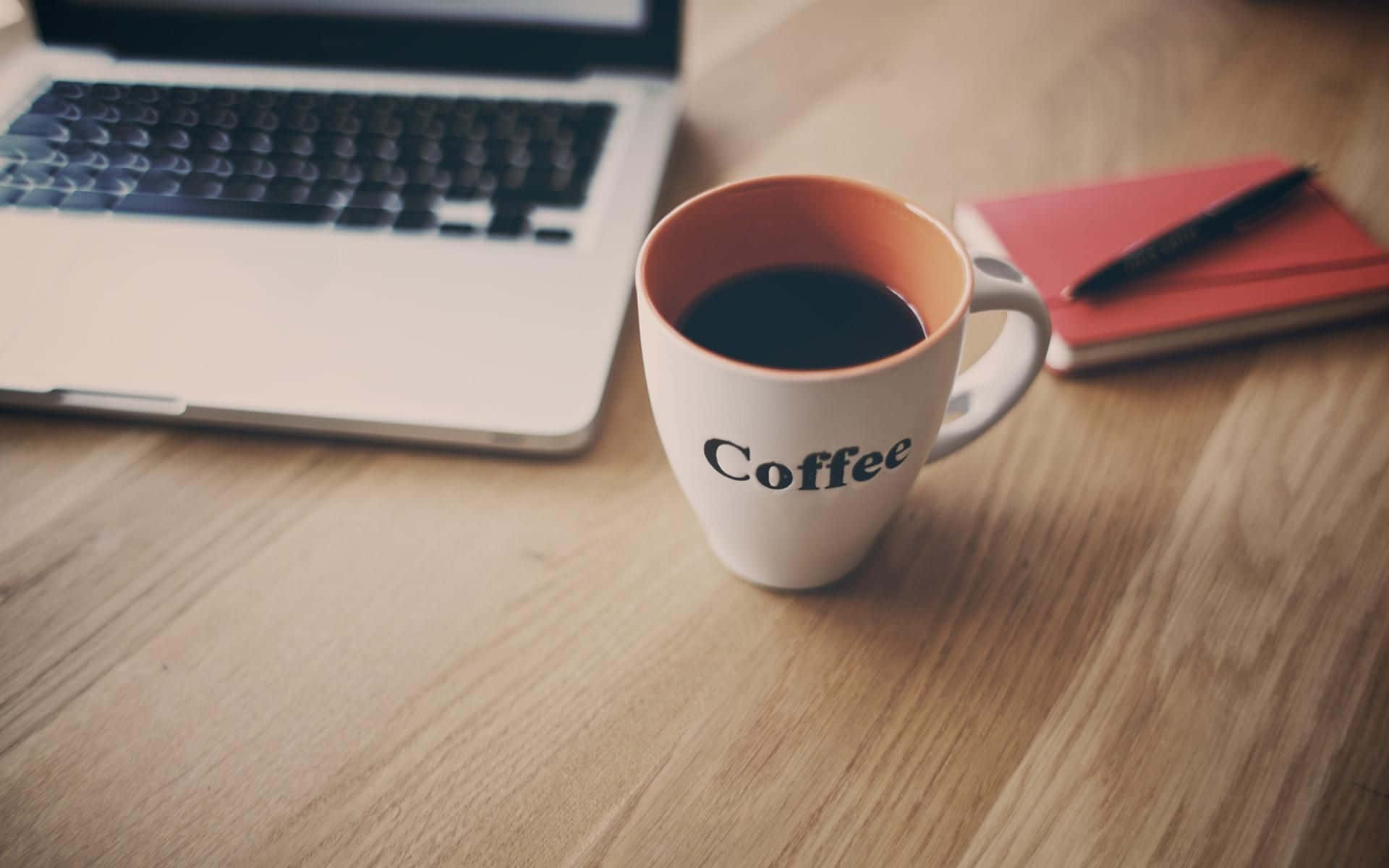 Coffee Aesthetic 桌布 壁紙 — 一個白色咖啡杯放在木桌上，旁邊有一台筆記型電腦和一本紅色筆記本，營造出舒適的工作空間。