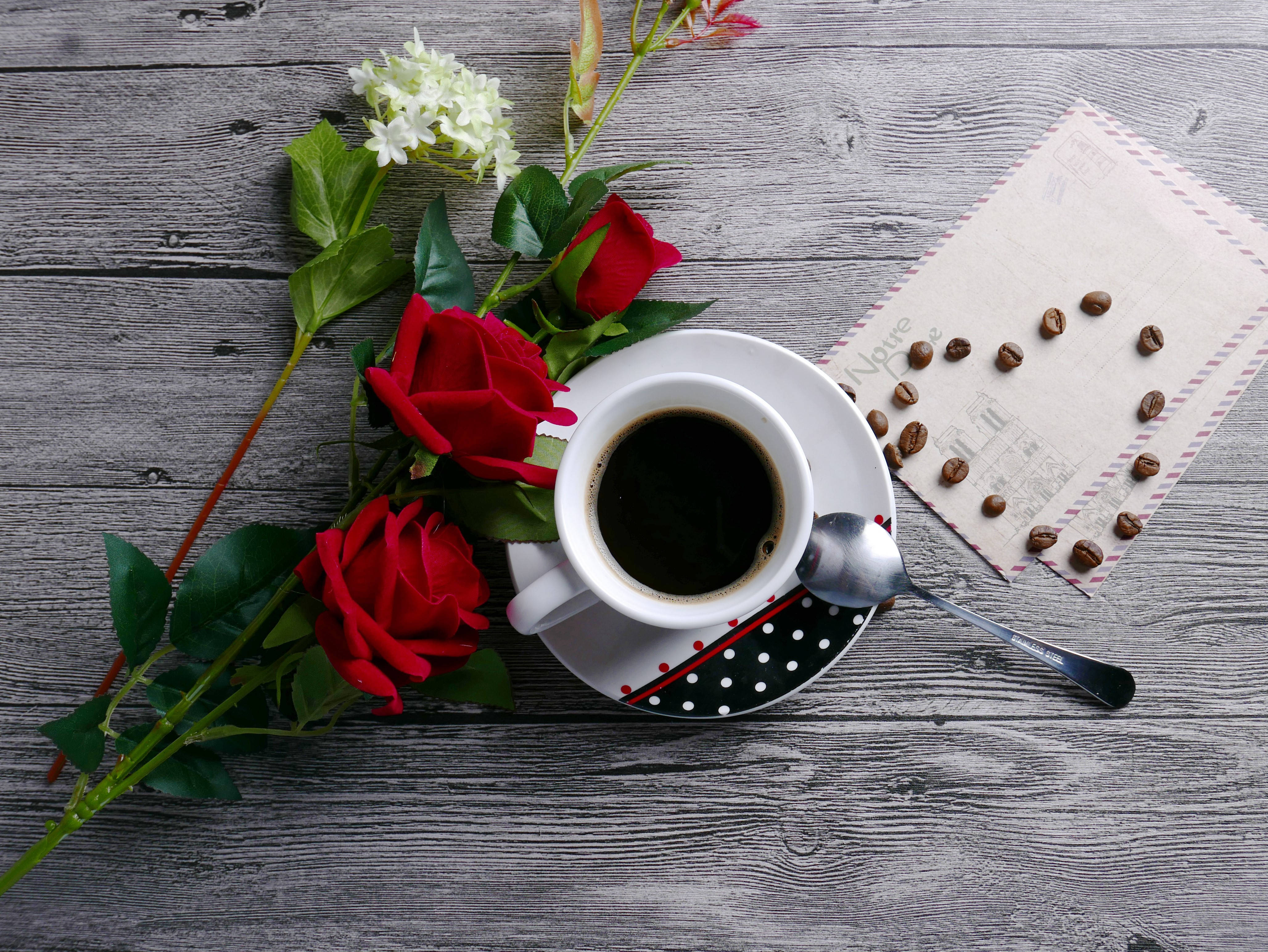 Coffee Aesthetic 桌布 壁紙 — 一個白色咖啡杯裝著深色咖啡，旁邊有紅玫瑰和散落的咖啡豆，放在一張風化的木桌上。