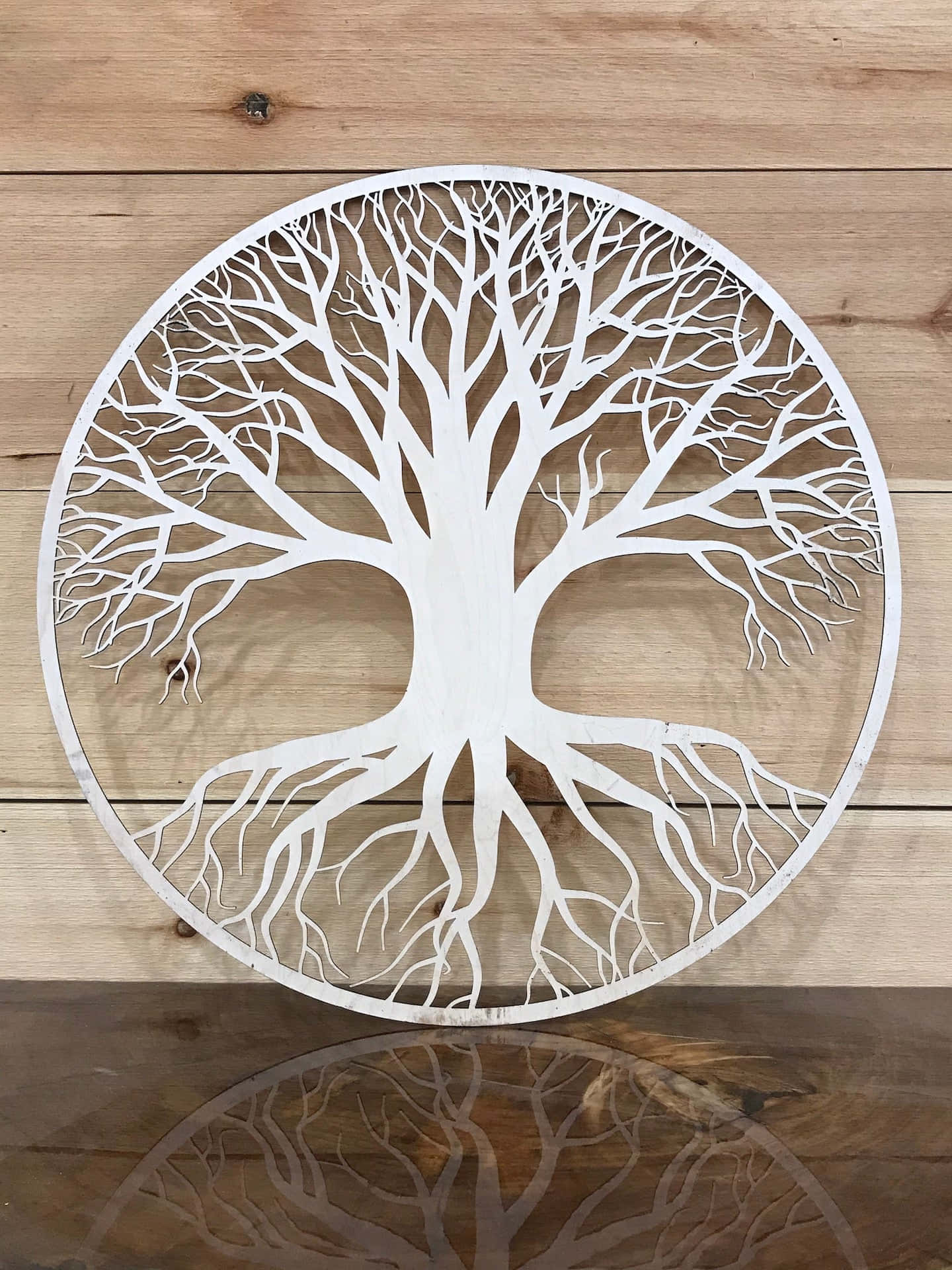 Tree Of Life 桌布 壁紙 — 一個白色圓形生命樹鏤空剪影，帶有複雜的根部和樹枝，安裝在木牆上，下方有反射表面。