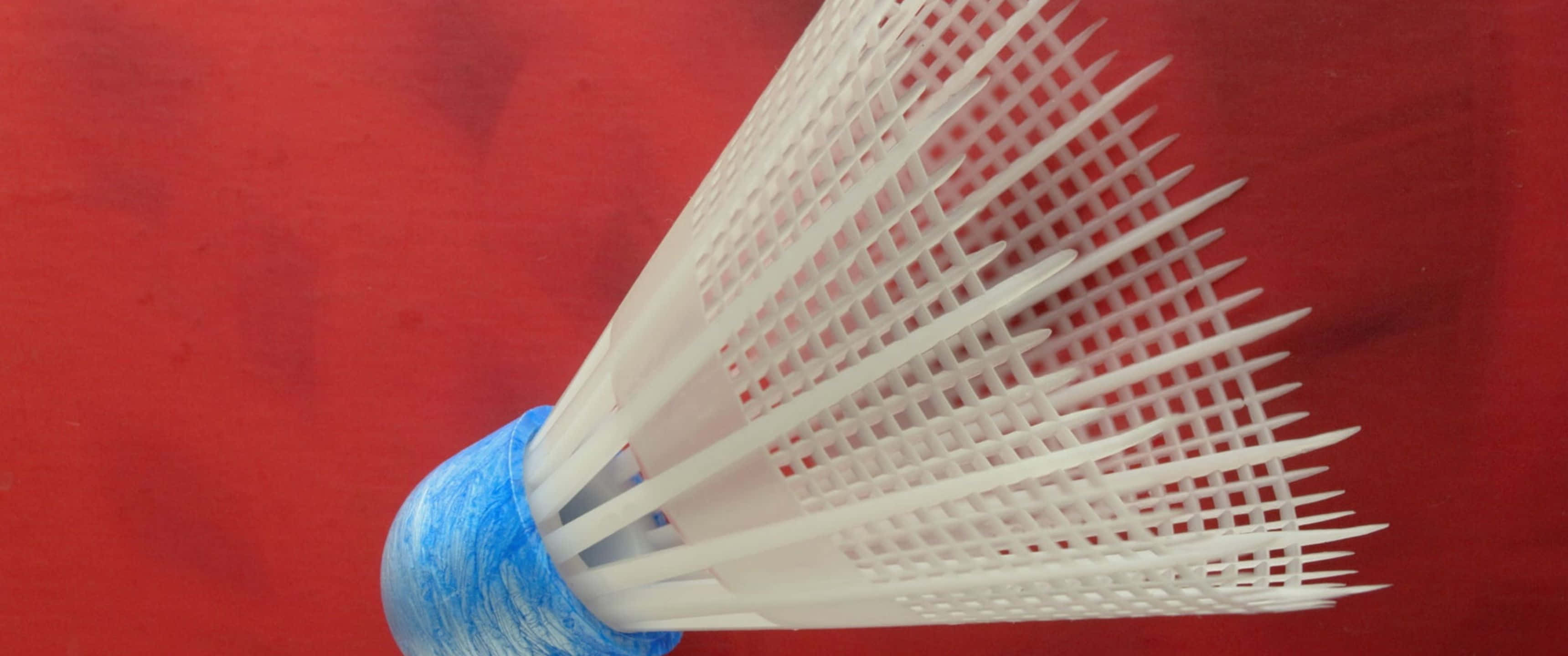 3440x1440p Badminton 桌布 壁紙 — 一個白色塑膠羽毛球近距離特寫，帶有藍色紋理底座，背景為鮮紅色。