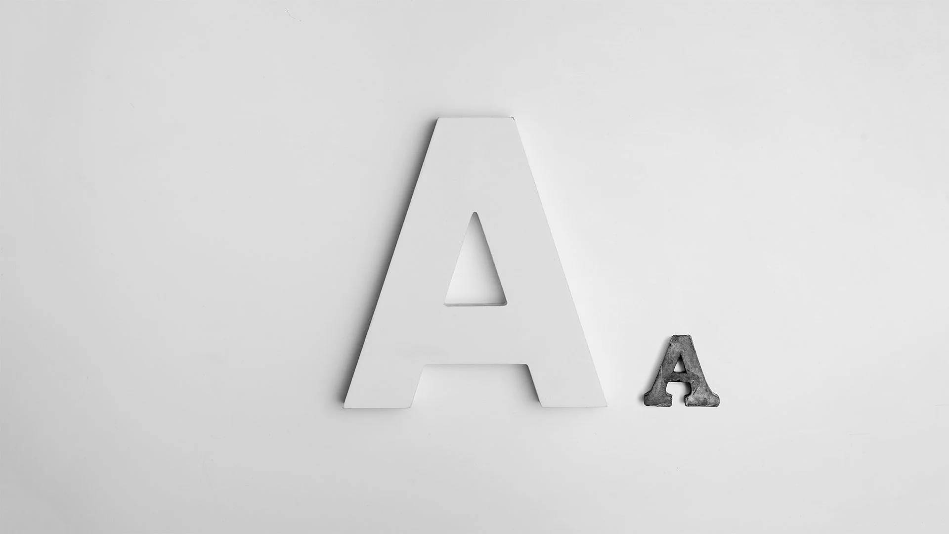 A 桌布 壁紙 — 一個白色大寫字母A旁邊有一個細小風化的小寫字母a，位於純淺灰色表面上。
