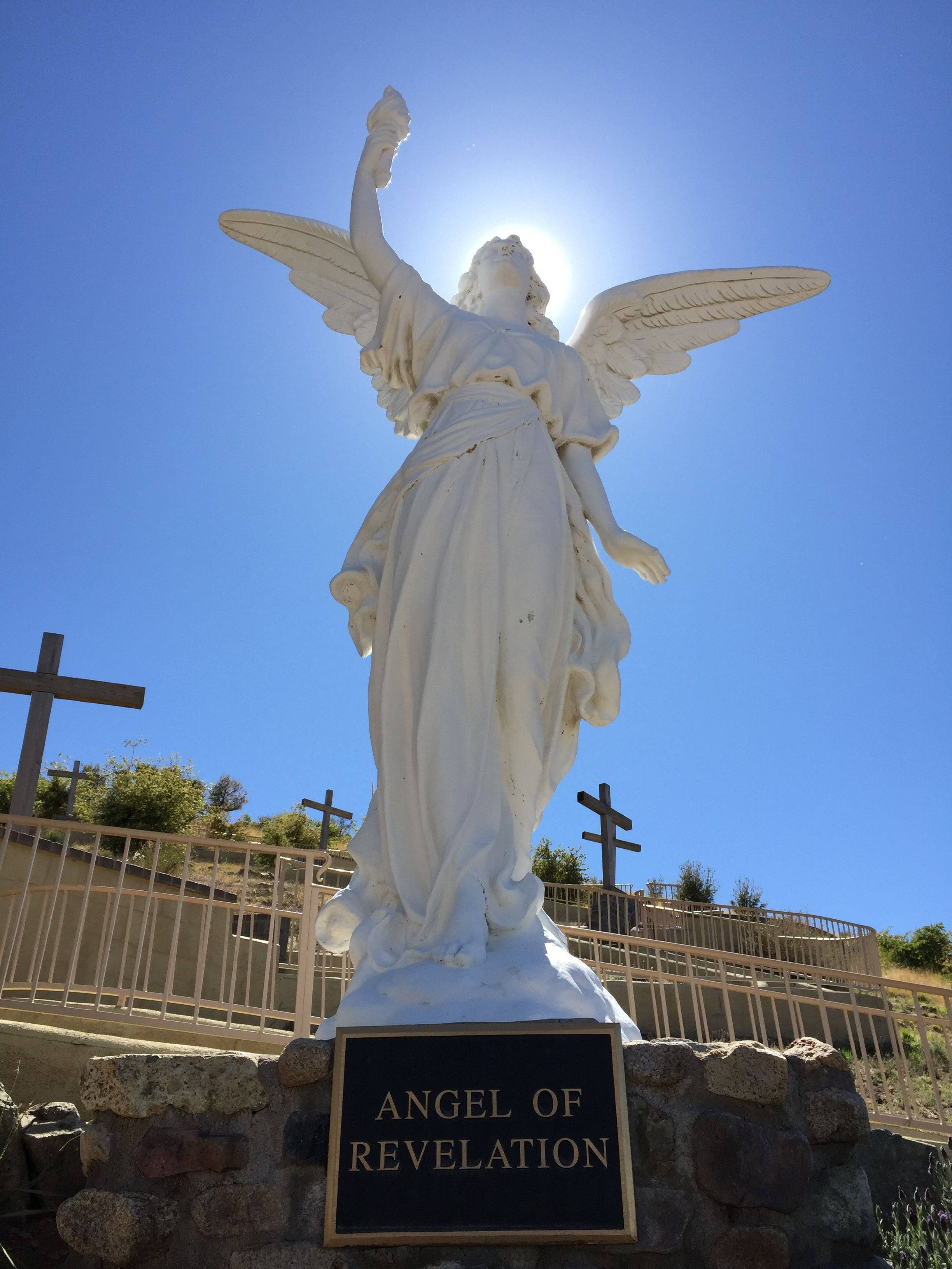 angels 桌布 壁紙 — 一個白色天使雕像展開翅膀，站在石基座上，在明亮的陽光下，被墓園中的十字架包圍。