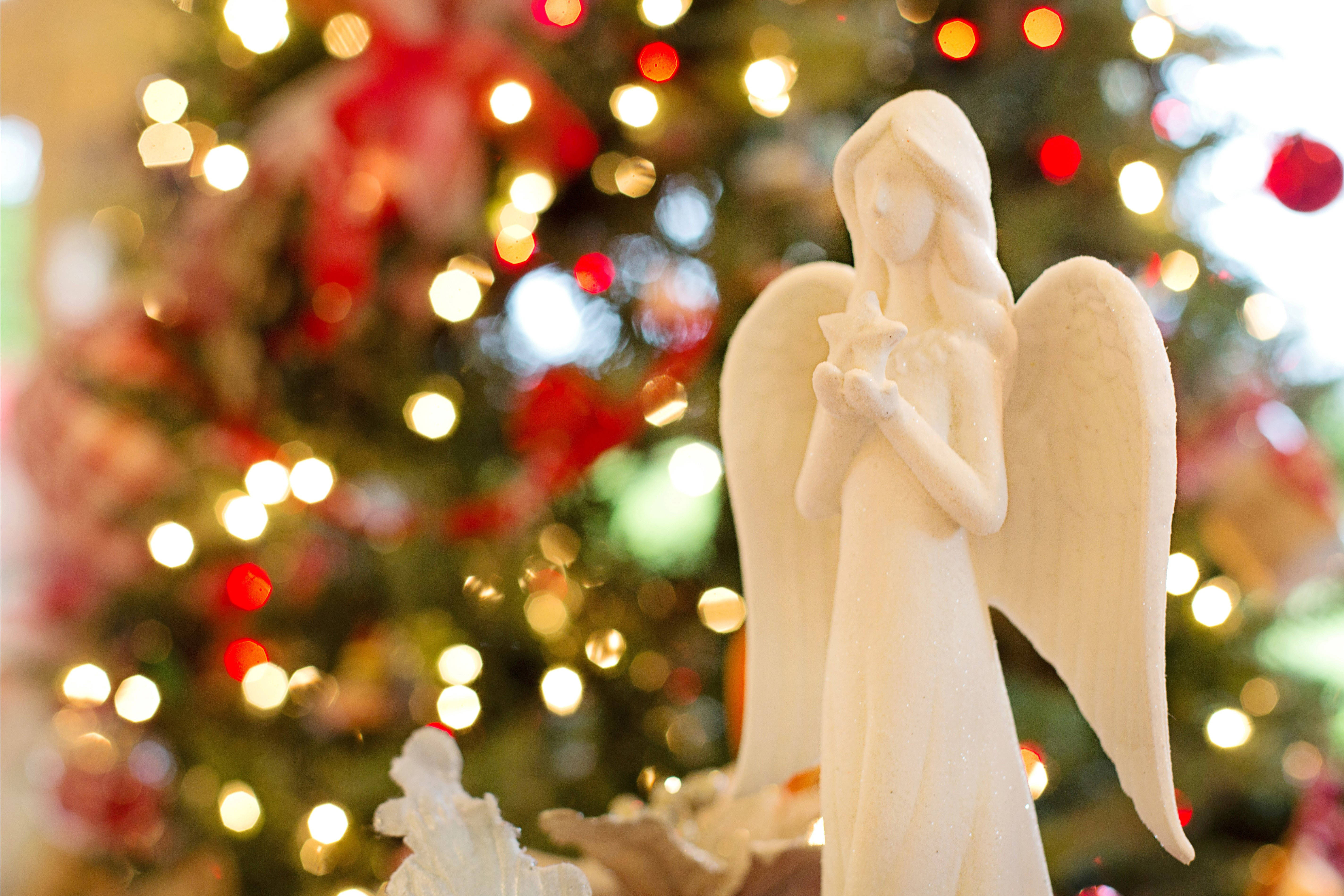 angels 桌布 壁紙 — 一個白色天使雕像手持星星，背景是柔和模糊、閃爍著溫暖燈光和紅色裝飾的聖誕樹。