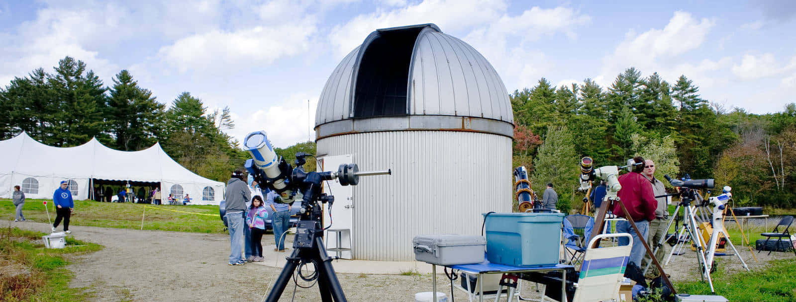 Observatory 桌布 壁紙 — 一個白色天文台圓頂帶有開放狹縫，矗立在草地上，天文愛好者在部分多雲的天空下使用望遠鏡。