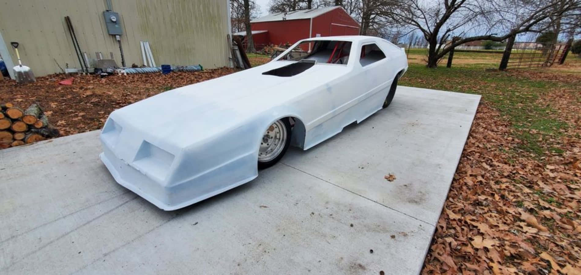 Funny Car 桌布 壁紙 — 一個白色定制賽車外殼放置在混凝土墊上，周圍有落葉和鄉村建築。