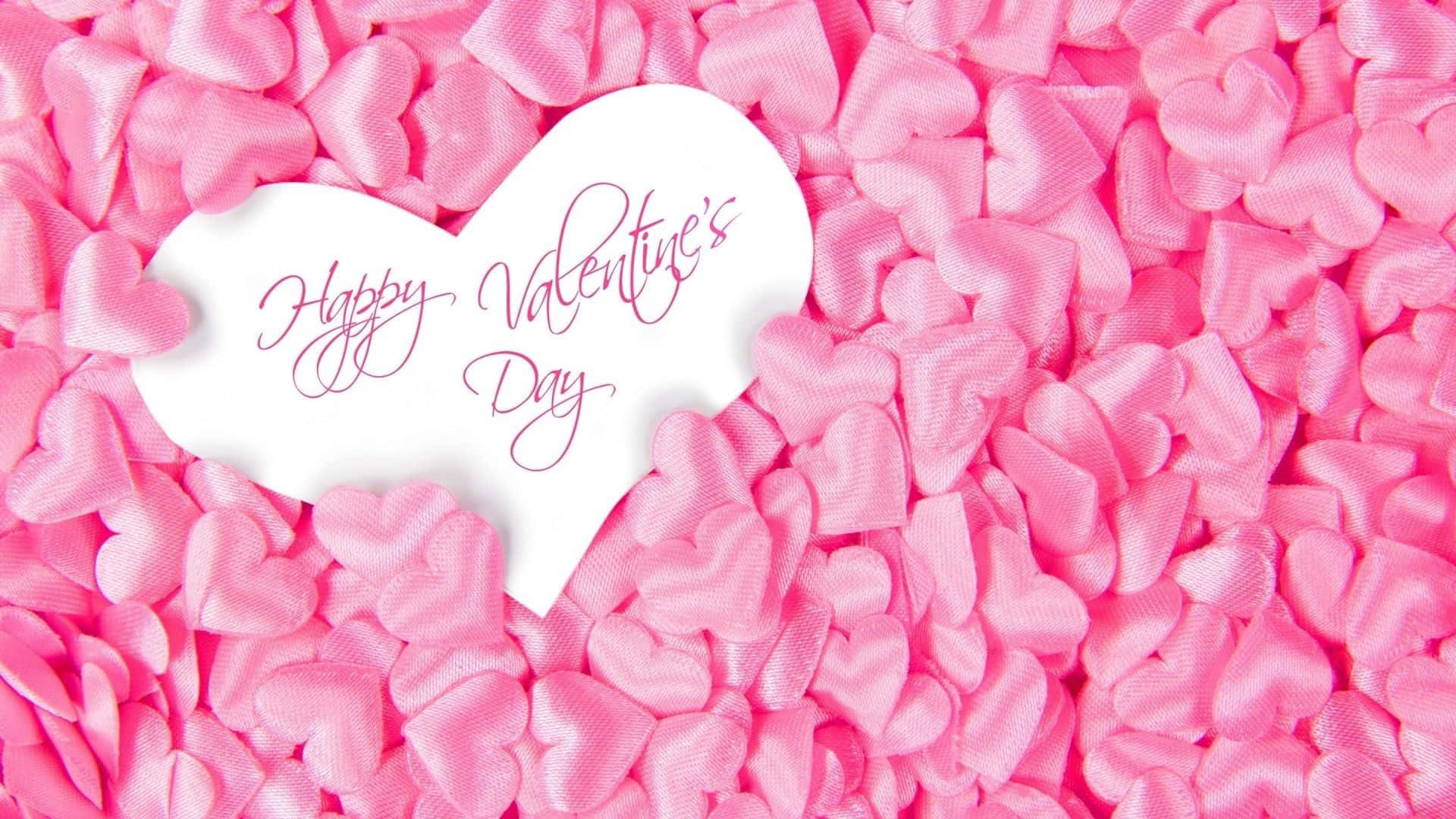 情人節 桌布 壁紙 — 一個白色心形，上面有草書Happy Valentine's Day文字，放在粉紅色緞面心形紙屑床上。