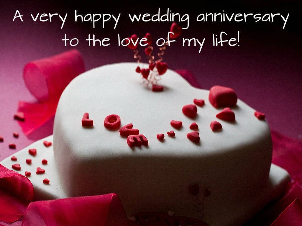 Happy Anniversary 桌布 壁紙 — 一個白色心形蛋糕，上面裝飾著紅色翻糖心形和 LOVE 字樣，周圍環繞著粉紅色絲帶，背景為深紫色。