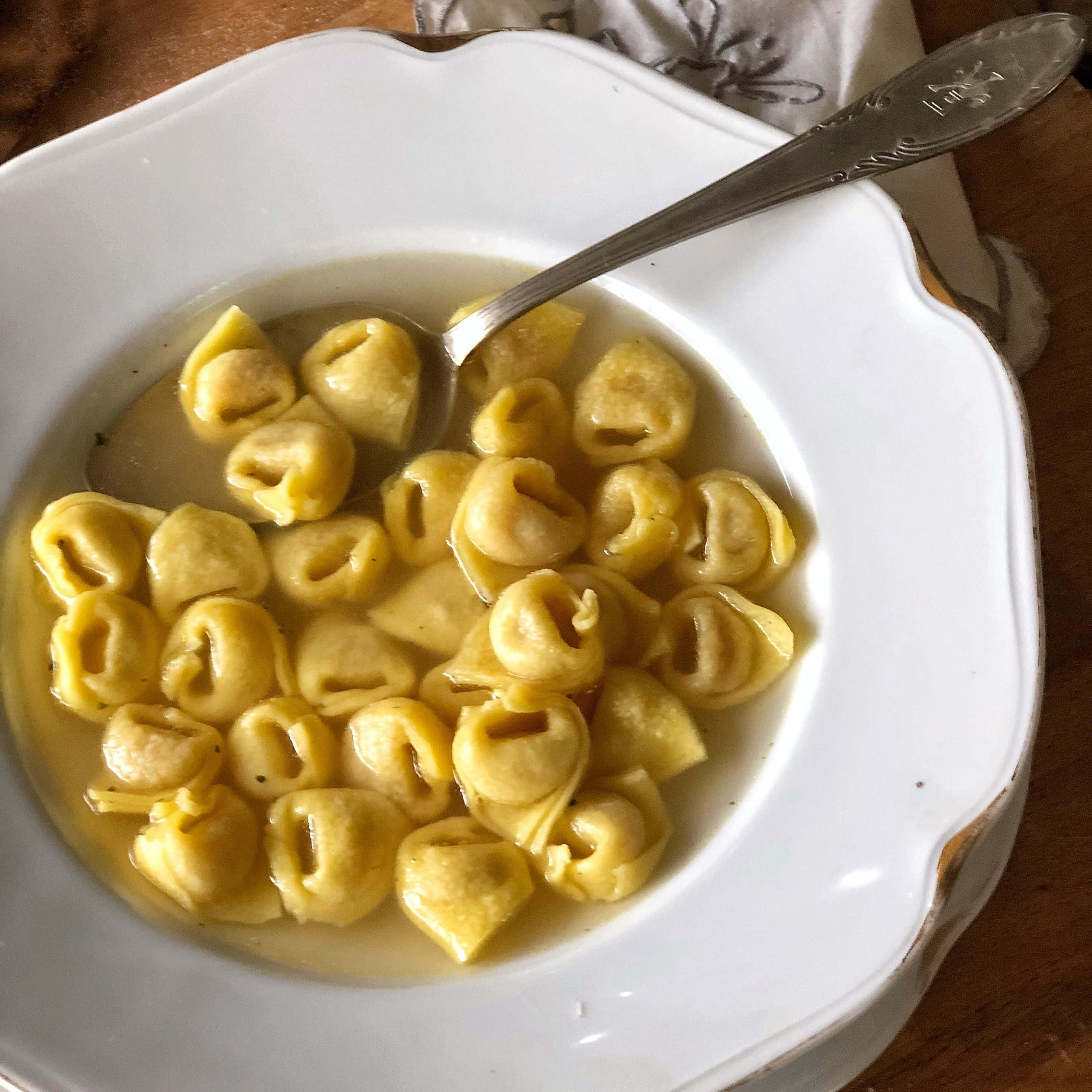 Pasta 桌布 壁紙 — 一個白色扇貝形碗，盛載著金黃色義大利雲吞在清湯中，內有銀匙。