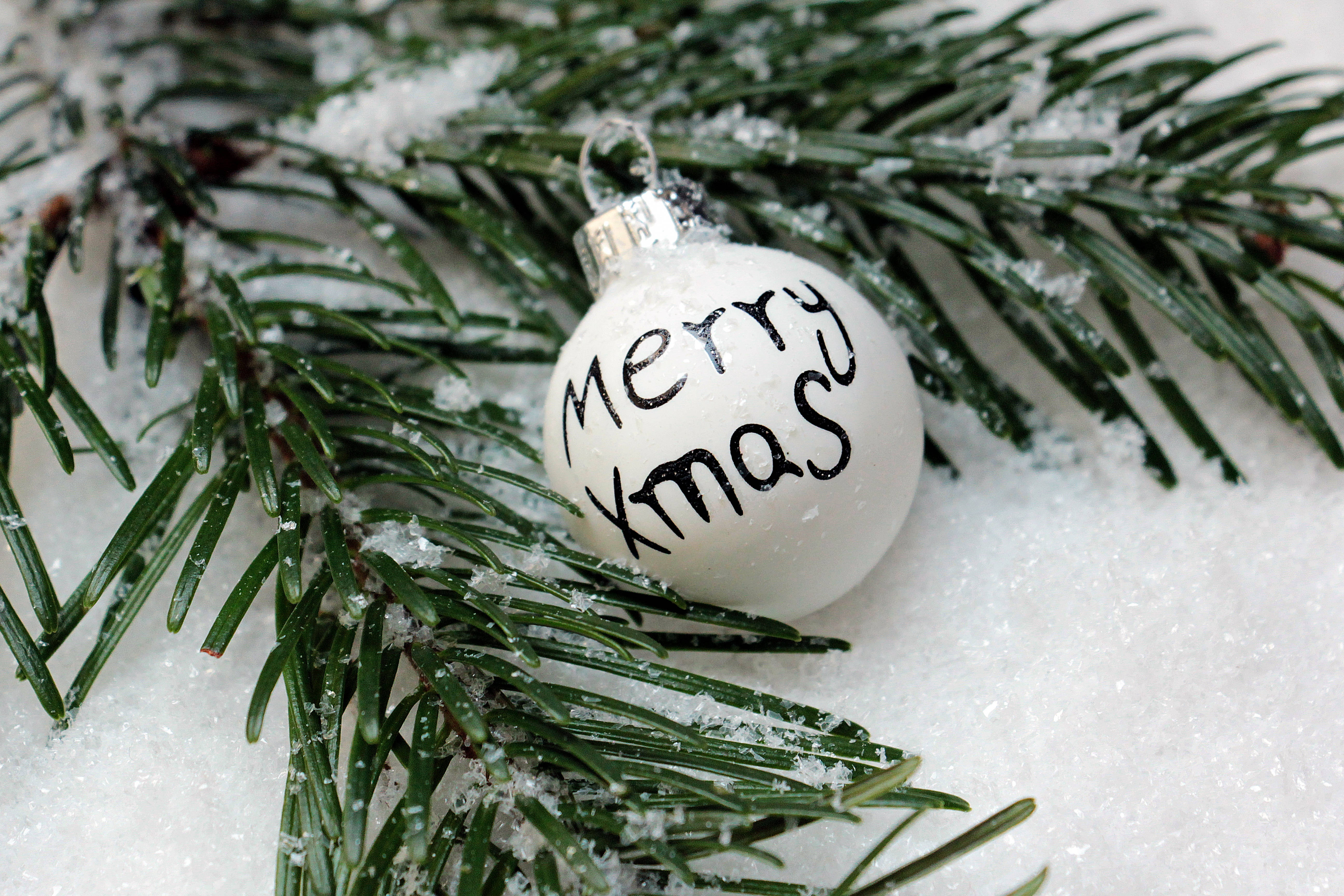 聖誕節 桌布 壁紙 — 一個白色手寫「Merry Xmas」裝飾品，藏在灑滿雪的常青樹枝中。