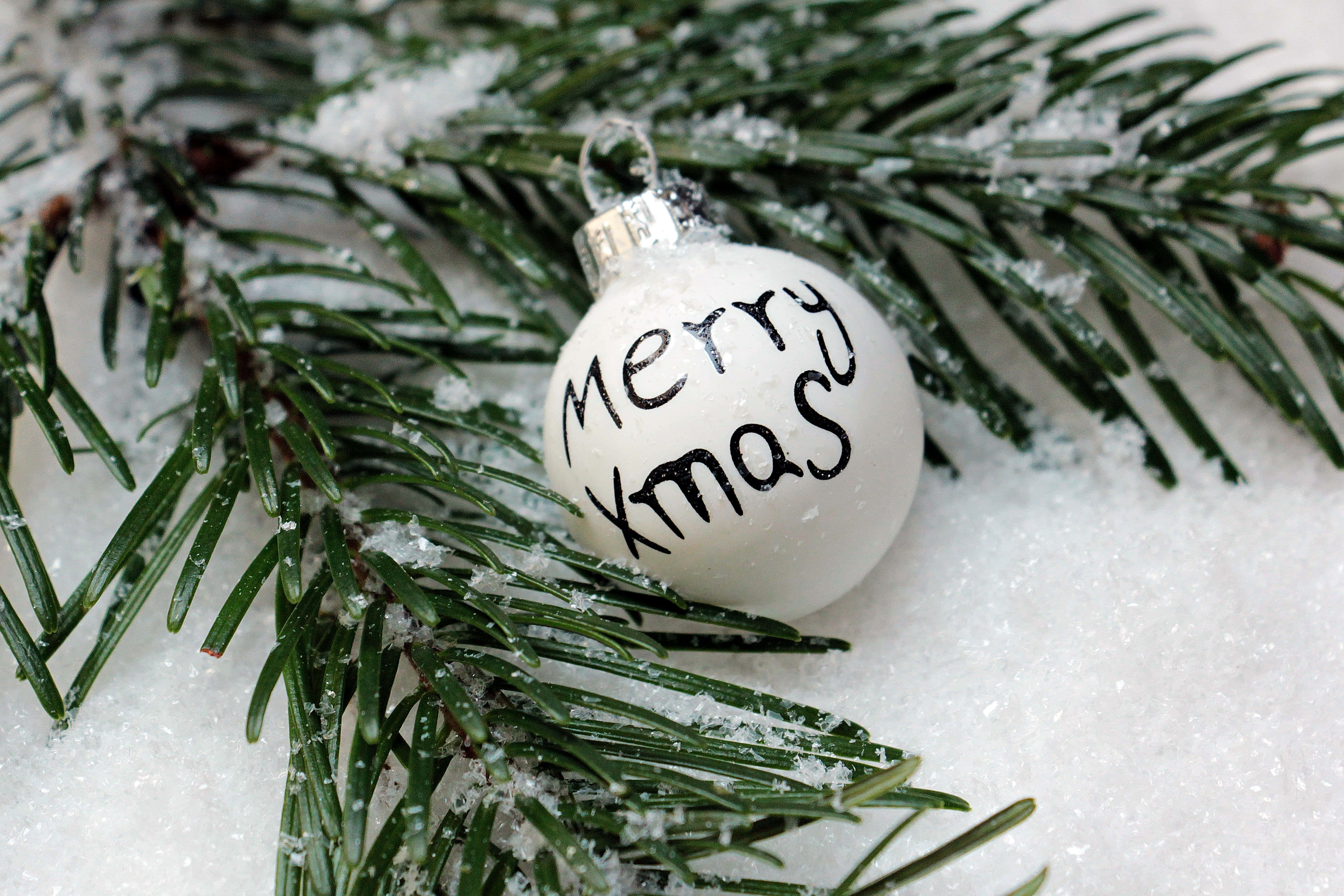 雪 桌布 壁紙 — 一個白色手寫「Merry Xmas」裝飾品放在灑滿白雪的常青樹枝上，構成清晰的冬日場景。