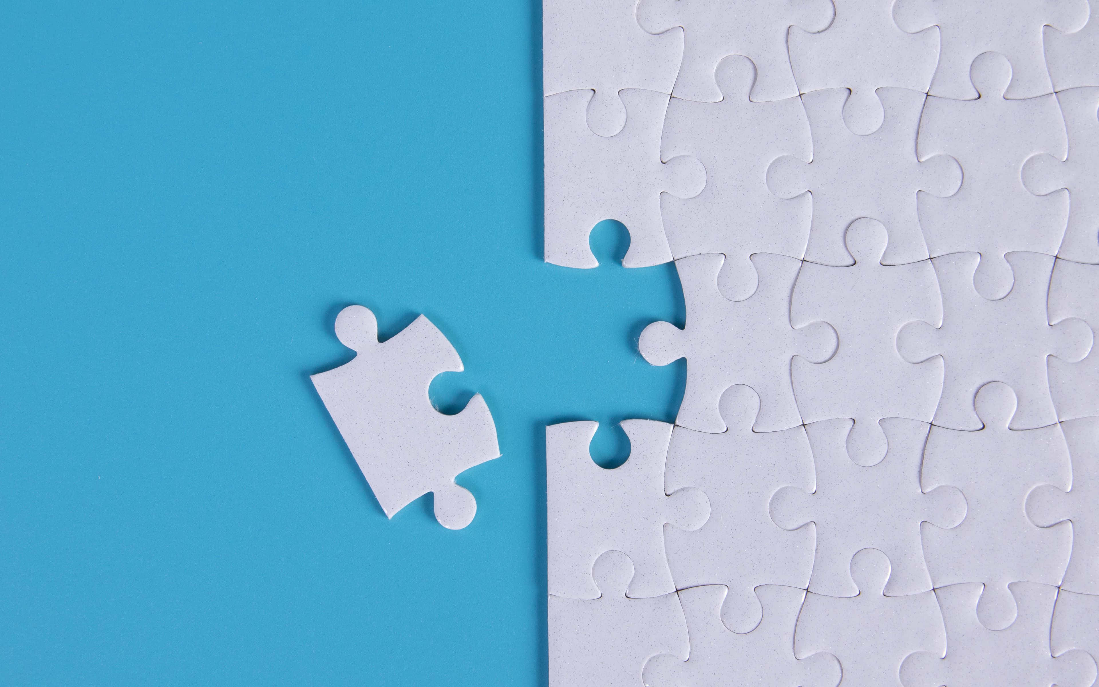 Puzzle 桌布 壁紙 — 一個白色拼圖塊漂浮在部分組裝的白色拼圖旁邊，背景為純藍色。