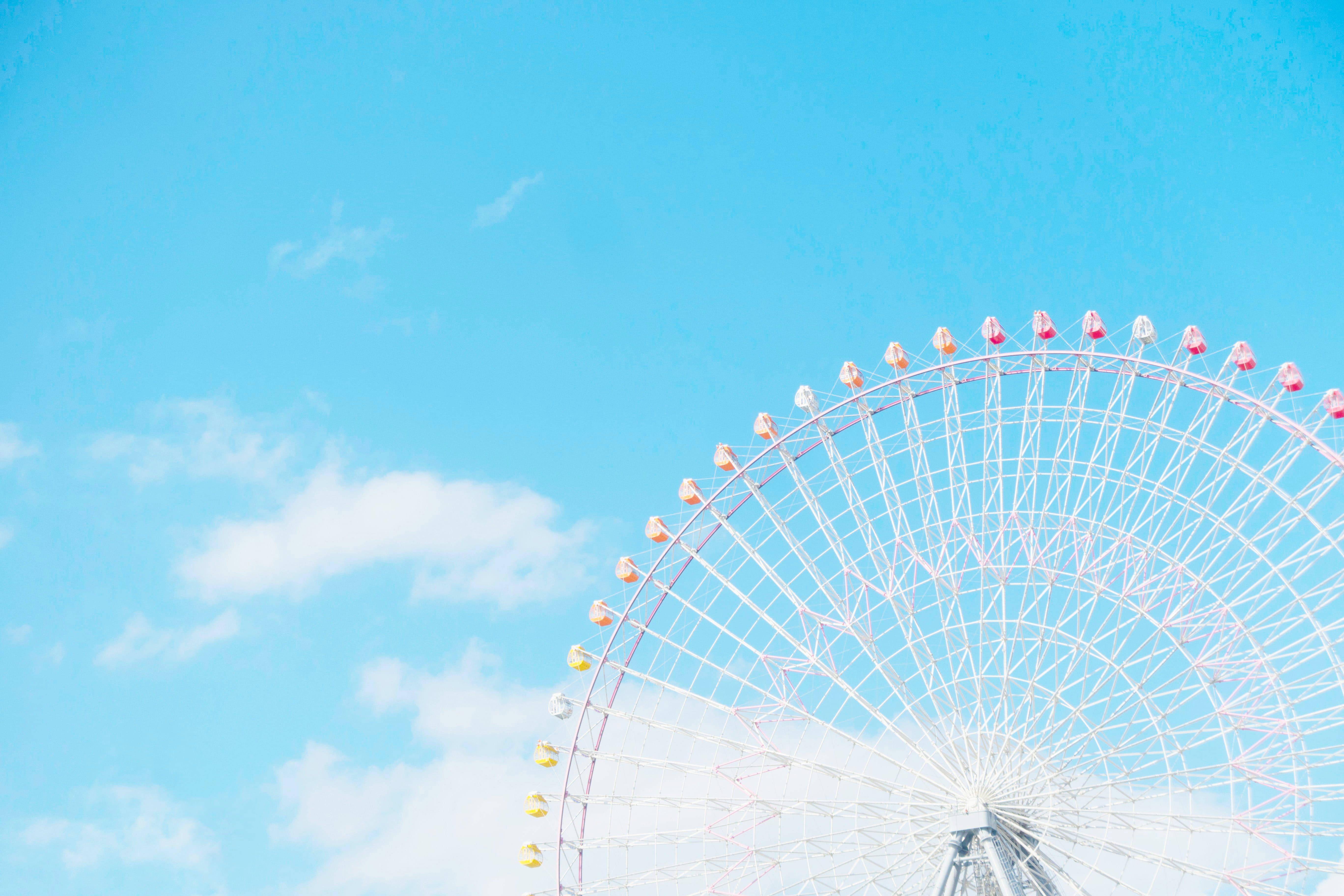 Theme Park 桌布 壁紙 — 一個白色摩天輪帶有色彩繽紛的車廂，在晴朗藍天和柔和白雲的襯托下彎曲。