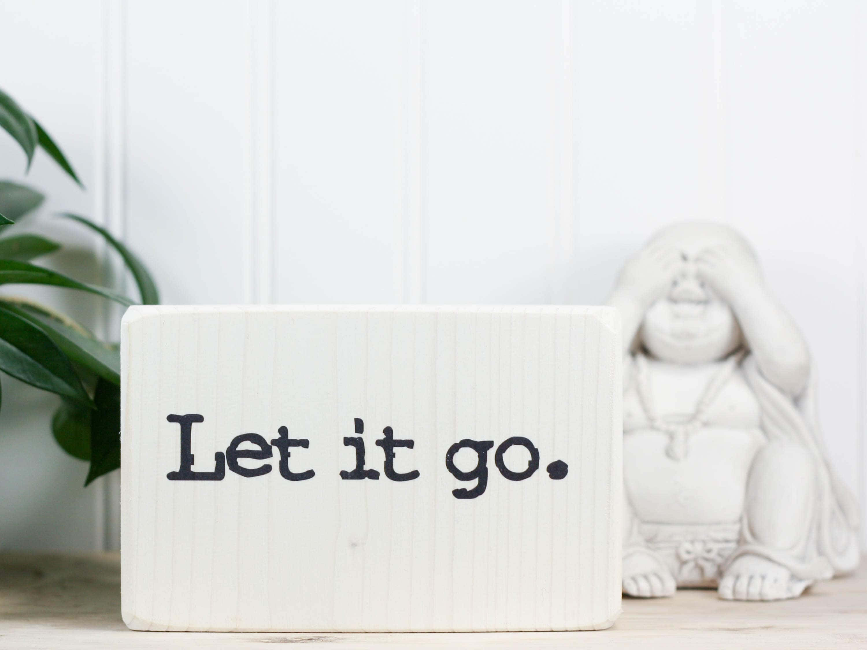 let it go 桌布 壁紙 — 一個白色木塊上寫著「Let it go」，旁邊有一個佛像和綠色植物，背景是白色鑲板牆。