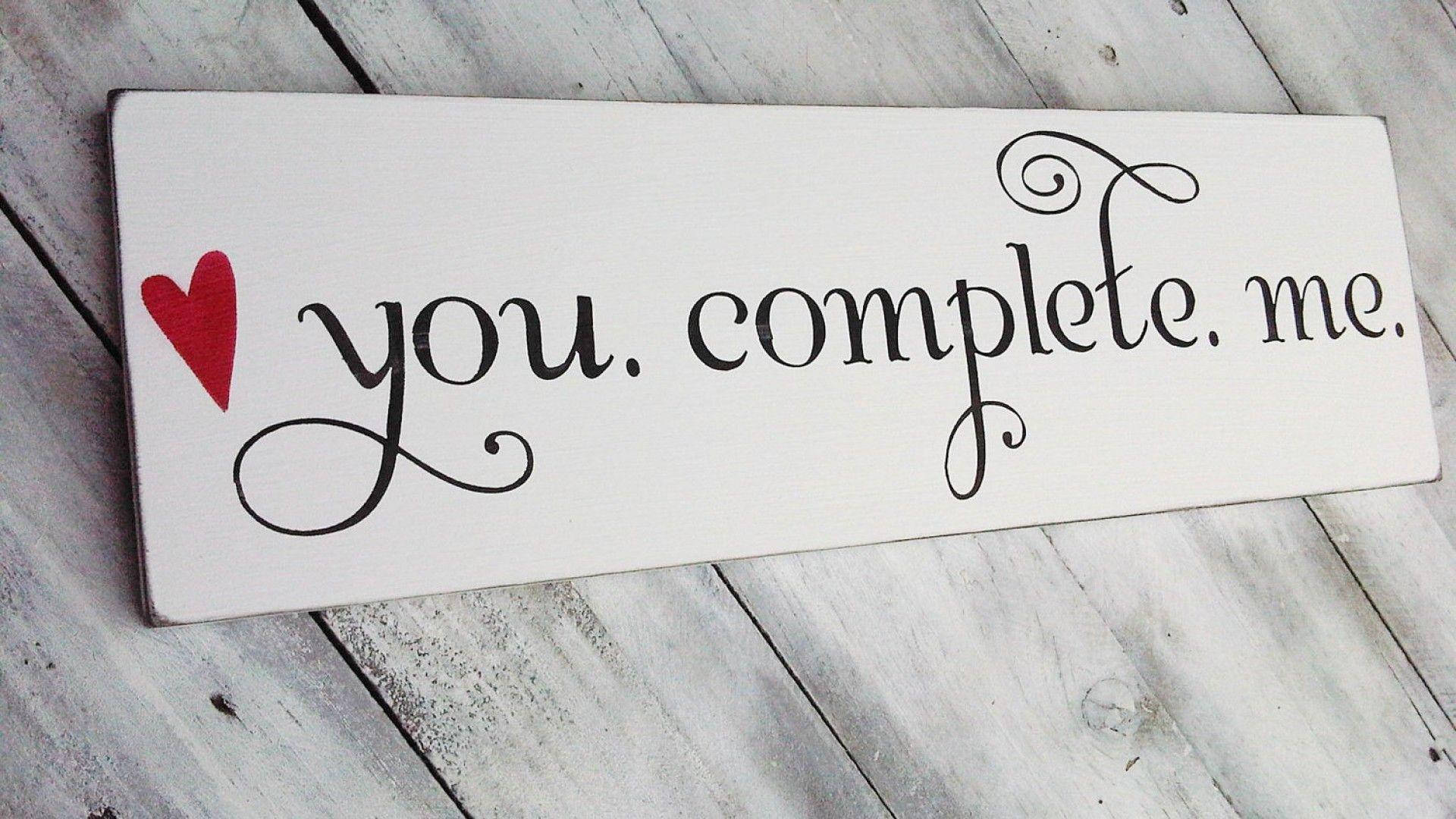 愛情語錄 桌布 壁紙 — 一個白色木牌，上面有黑色草書文字寫著「you complete me」和一個紅色愛心，放在經風化的灰色木頭上。