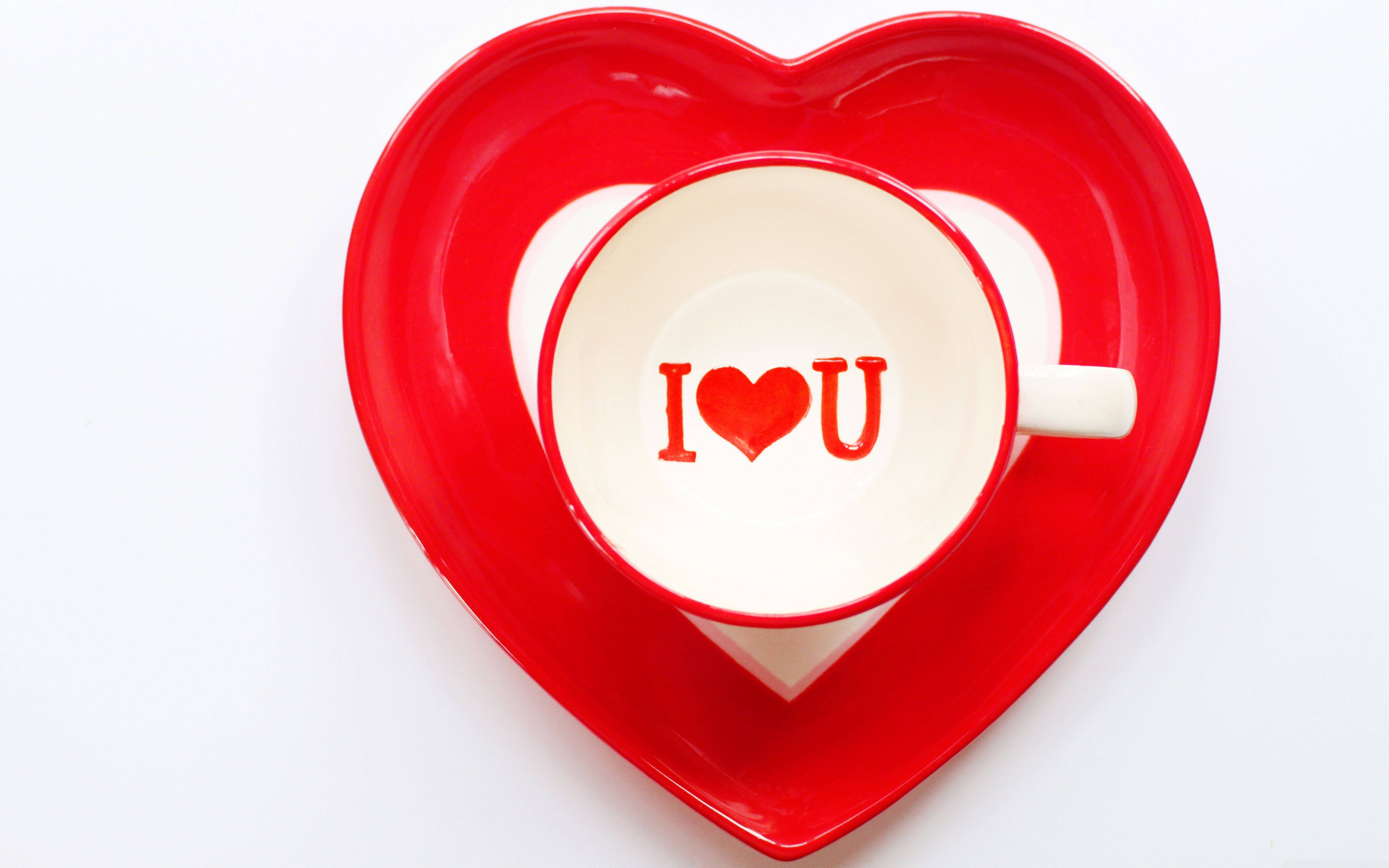 I Love You Aesthetic 桌布 壁紙 — 一個白色杯子帶有紅色I heart U文字，放在一個光滑的紅色心形碟子上，背景是乾淨的白色。