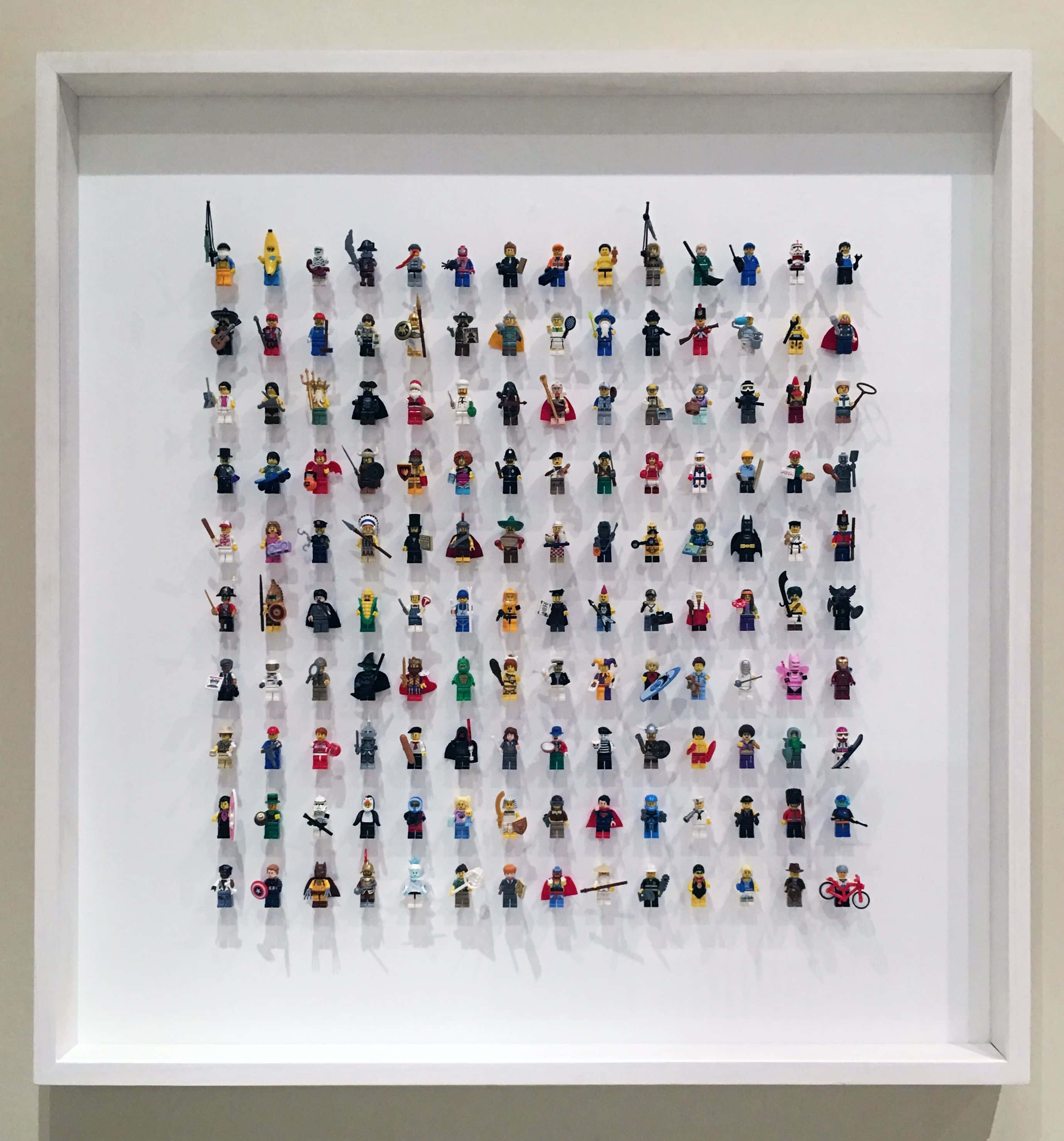 Lego Art 桌布 壁紙 — 一個白色框的展示架整齊排列著數十個色彩繽紛的樂高迷你人偶，背景是純白色。