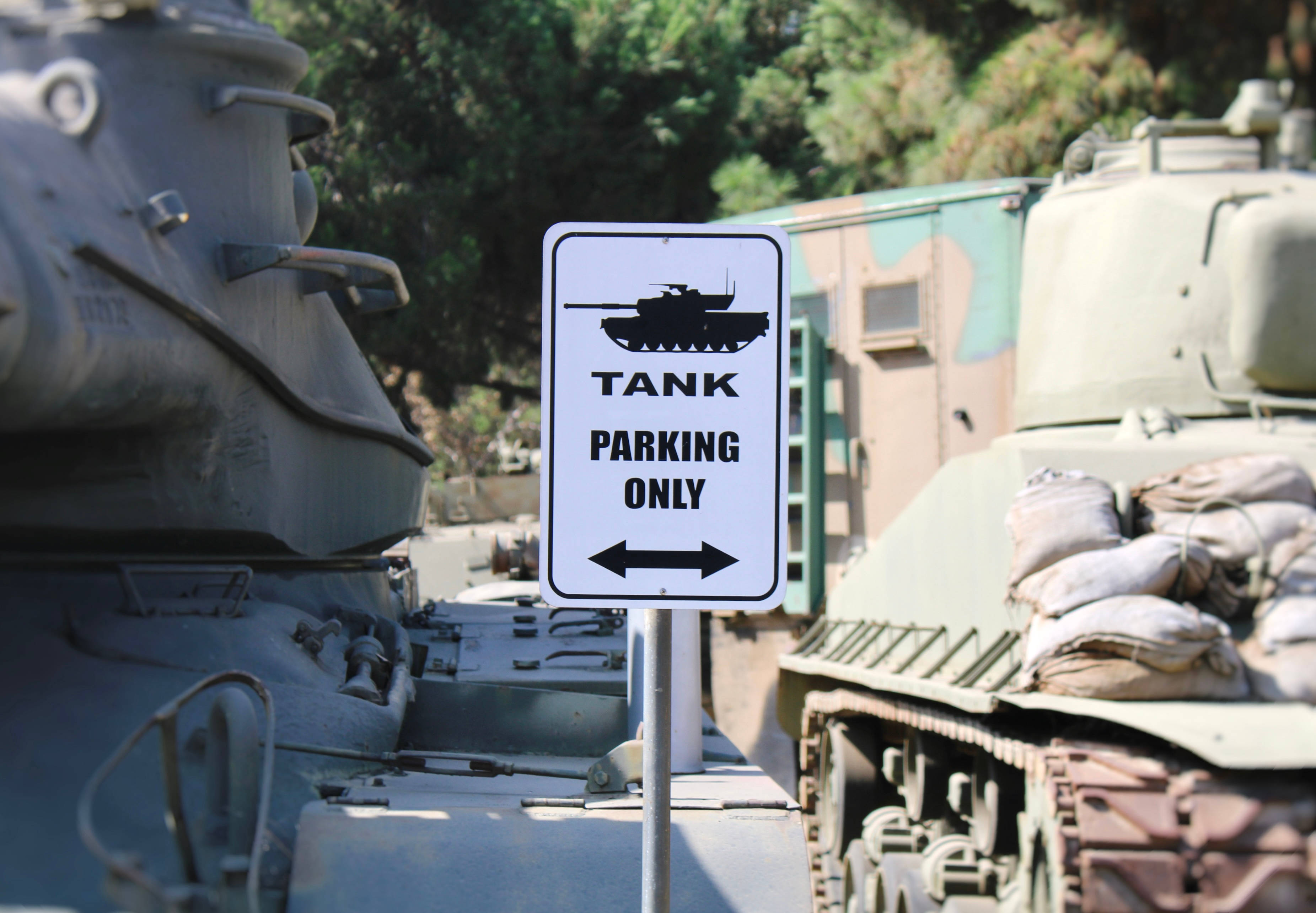Tanks 桌布 壁紙 — 一個白色標誌寫著「TANK PARKING ONLY」，在明亮的日光下矗立在兩輛軍用坦克之間。