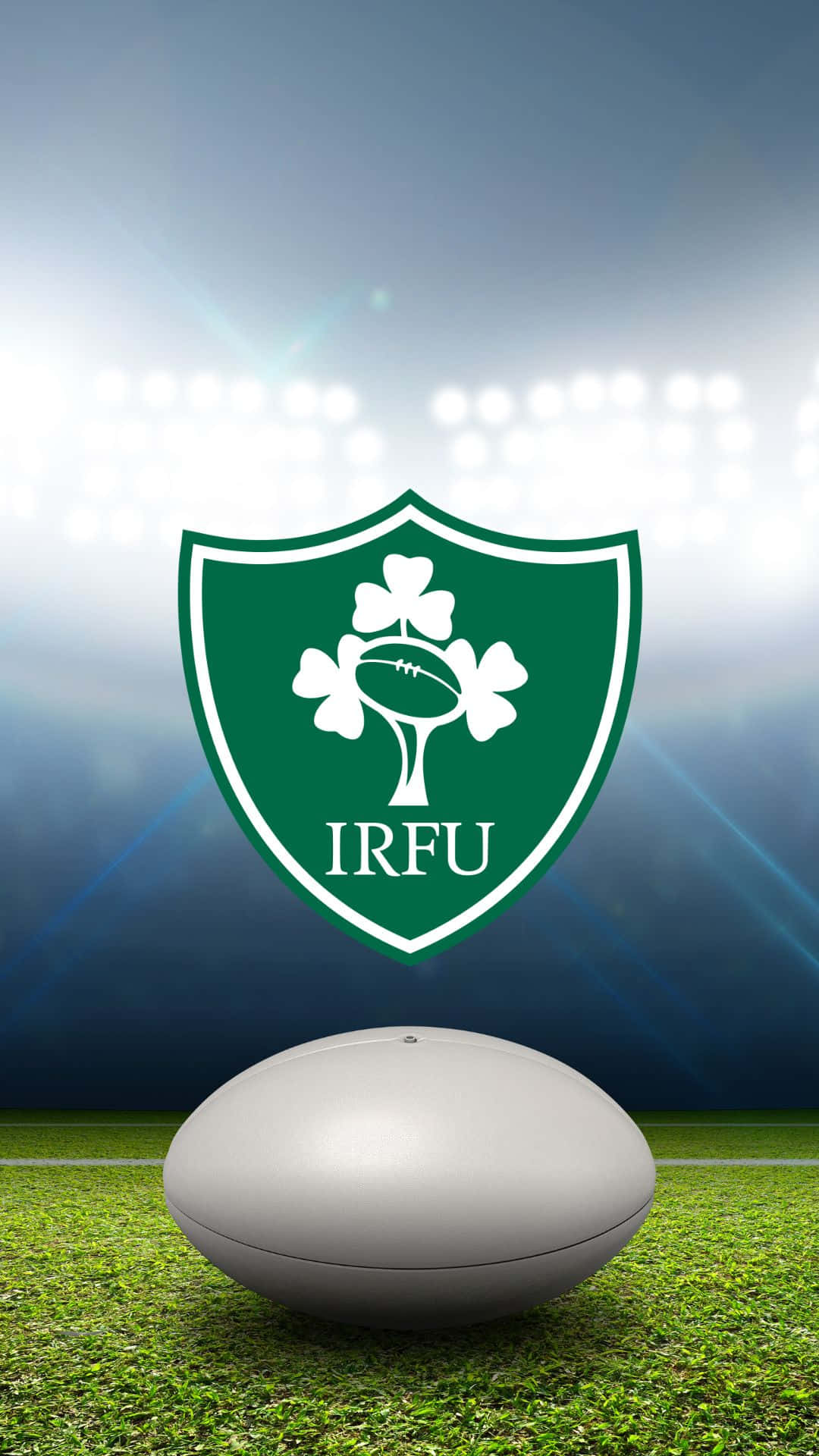 Ireland Rugby 桌布 壁紙 — 一個白色橄欖球放在充滿活力的綠色草地上，下方是愛爾蘭橄欖球聯盟標誌，被球場燈光照亮。