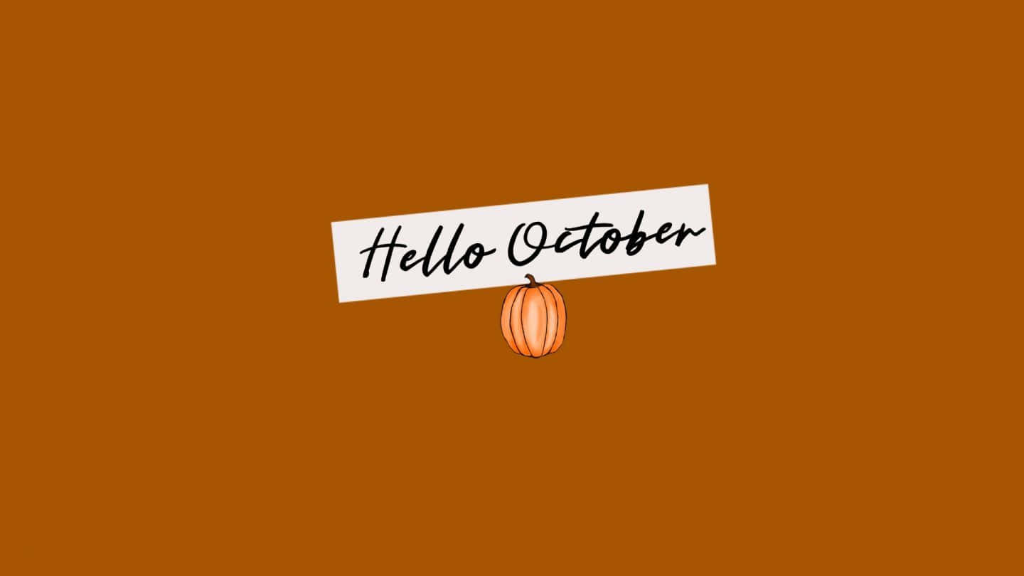 October 桌布 壁紙 — 一個白色橫幅上以草書寫著 Hello October，懸掛在一個小橙色南瓜上方，背景為純鏽色。