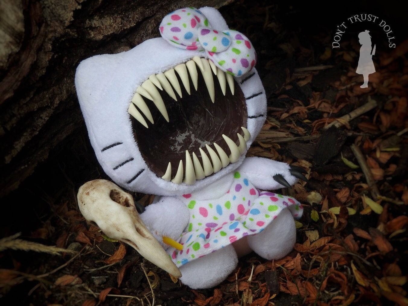 Hello Kitty Halloween 桌布 壁紙 — 一個白色毛絨玩具，類似Hello Kitty，有尖銳的牙齒，旁邊有一個骷髏頭，躺在落葉中。