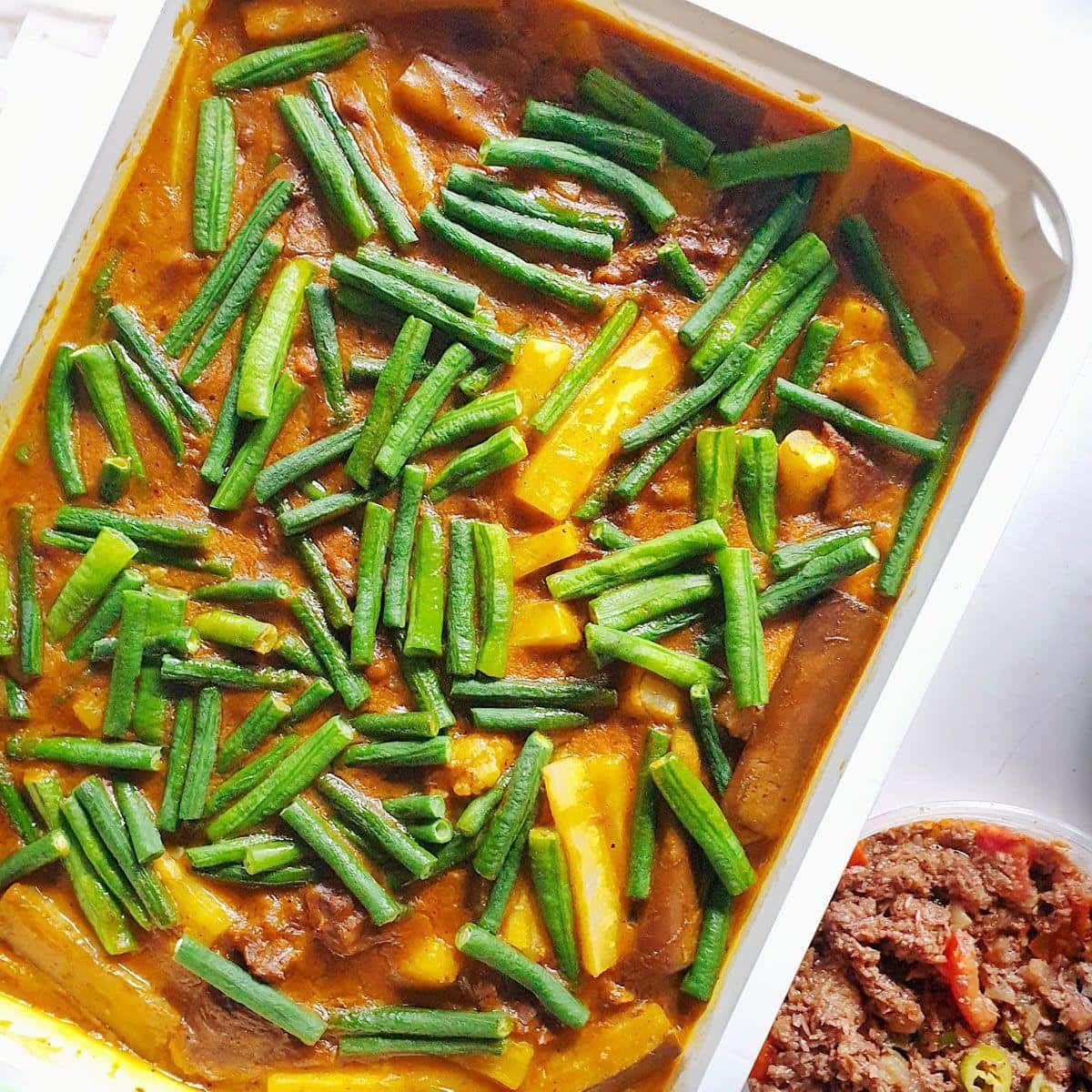 meat 桌布 壁紙 — 一個白色烤盤中，充滿活力的橙色咖哩配上綠色秋葵和黃色南瓜。