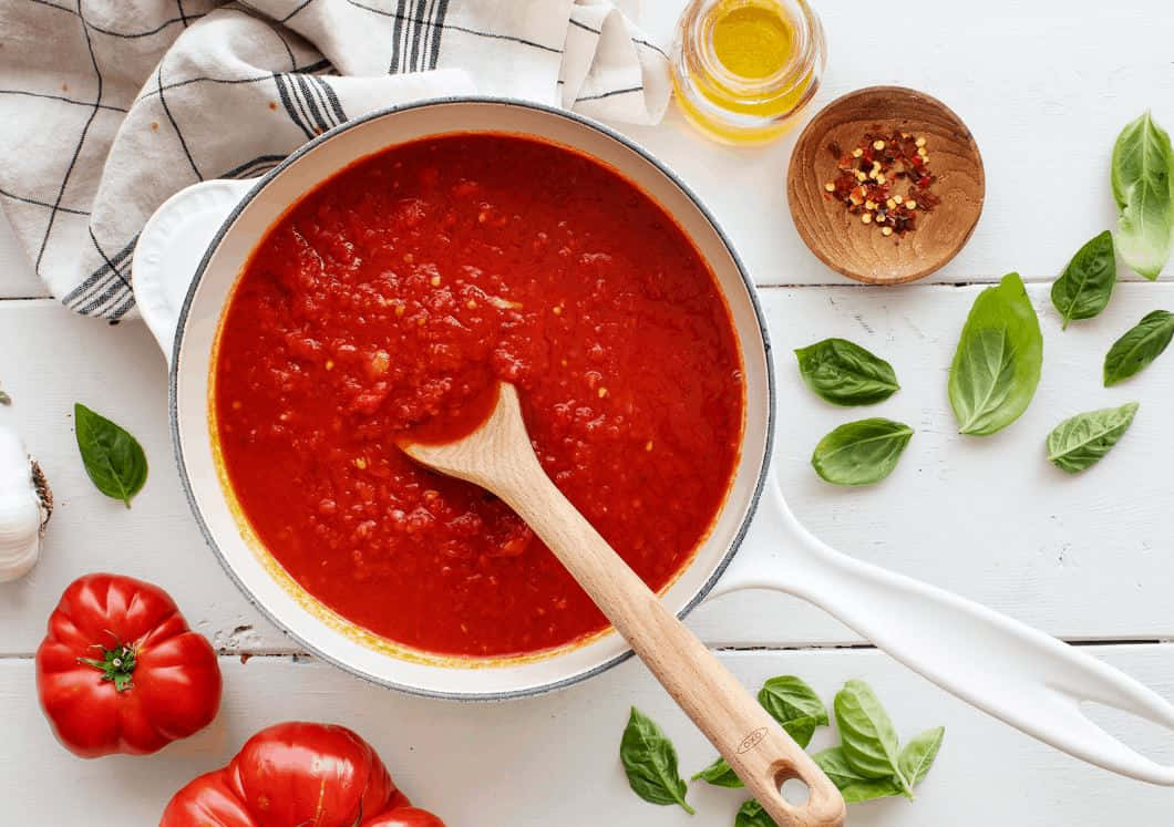 Red Sauce 桌布 壁紙 — 一個白色煎鍋裝滿了鮮紅色的番茄醬，放在白色木桌上，周圍是新鮮的羅勒葉、整個番茄和一瓶橄欖油。